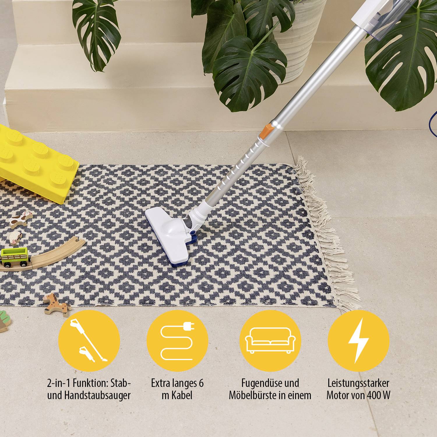 Ein weißer Stabstaubsauger auf einem blau-weißen Teppich, umgeben von Spielzeug; Werbung für 2-in-1 Funktionen und 6 m Kabel.