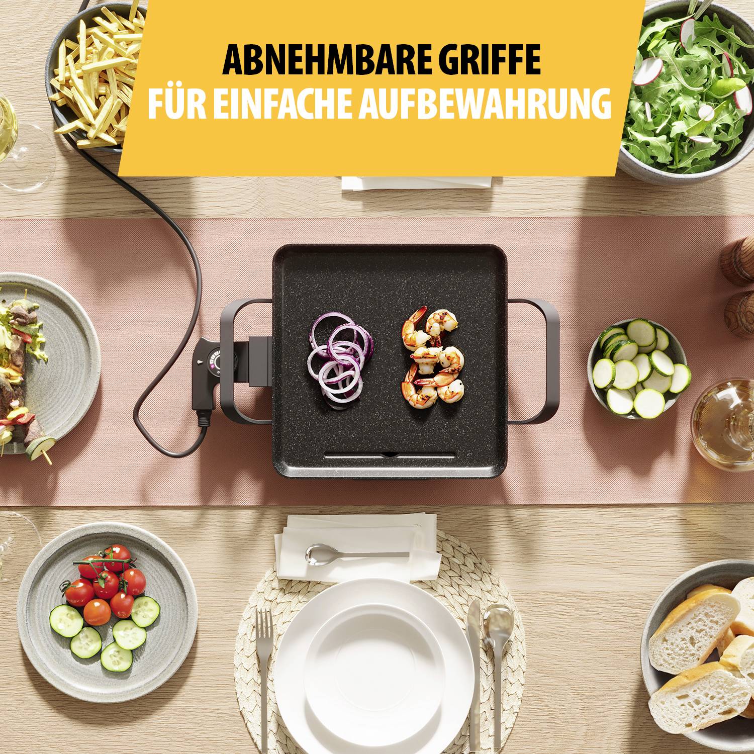 Tisch mit einem Grillgerät in der Mitte, darauf Garnelen und Zwiebeln. Umgeben von Tellern mit Beilagen. Oben Text: 'Abnehmbare Griffe für einfache Aufbewahrung'.