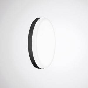 Runde, flache Wandleuchte mit schwarzem Rand, leuchtet in einem ansonsten leeren, weißen Raum.