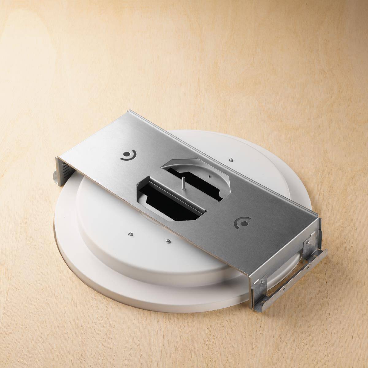 Ein rundes weißes Gerät mit einer silbernen Metallhalterung darauf. Es liegt auf einer Holzoberfläche.