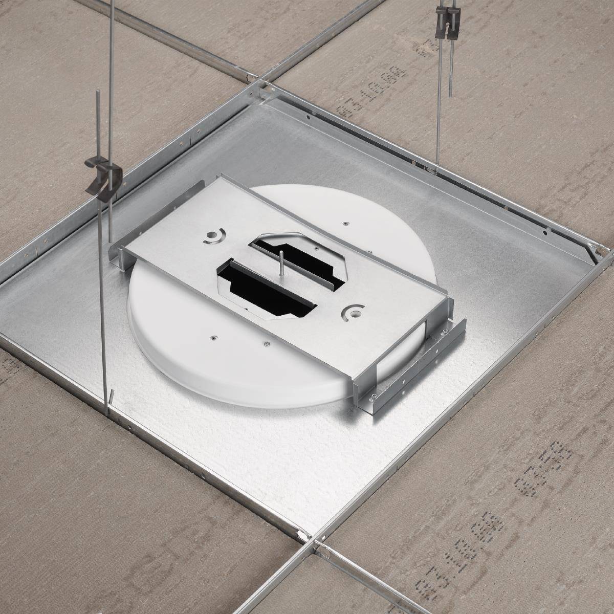 Eine Deckeninstallation mit einem runden Belüftungselement und einer Metallhalterung, zwischen Akustikplatten aufgehängt.