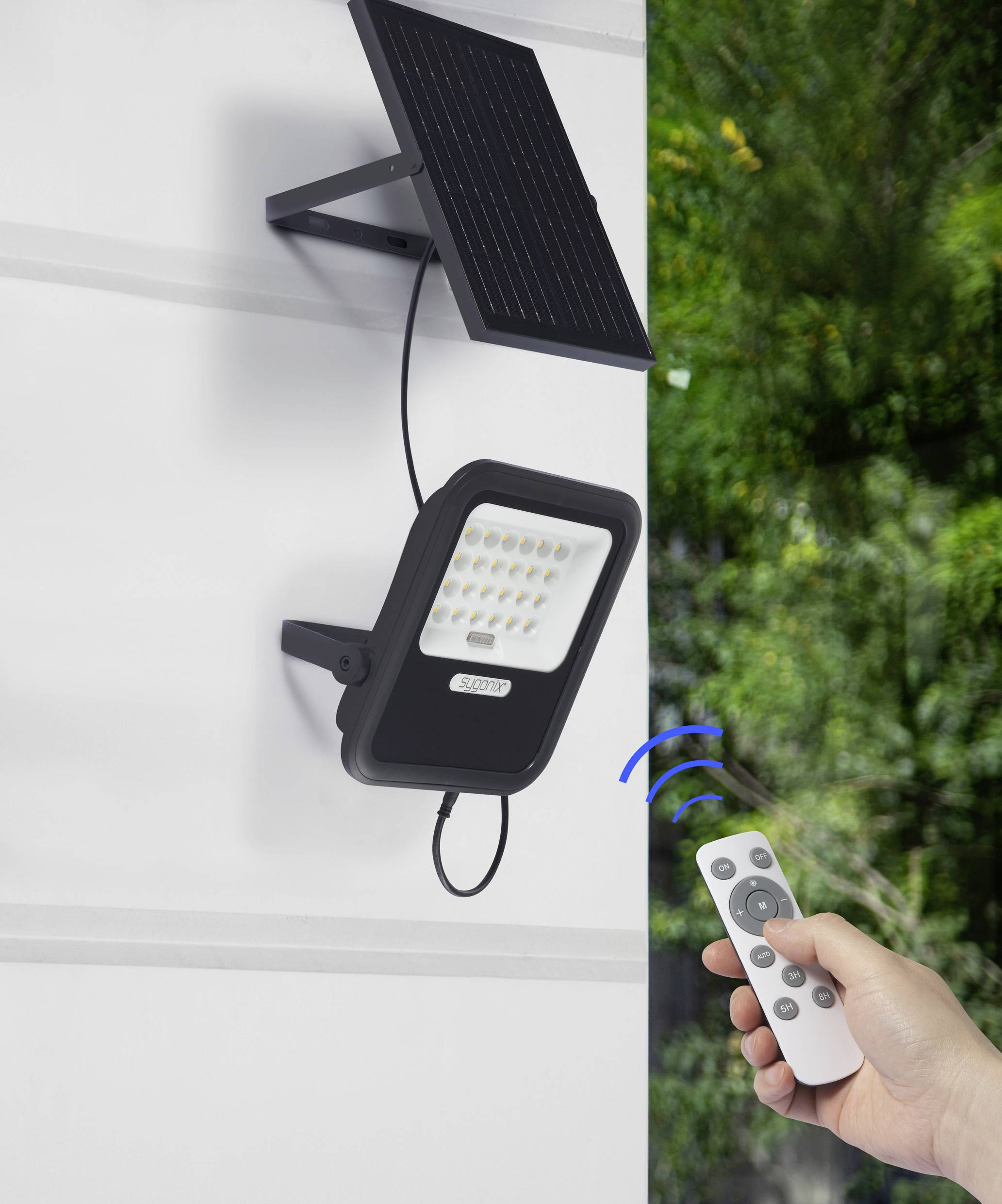 Solarbetriebene LED-Leuchte an einer Wand montiert, wird mit einer Fernbedienung im Vordergrund gesteuert. Hintergrund: grüne Pflanzen.