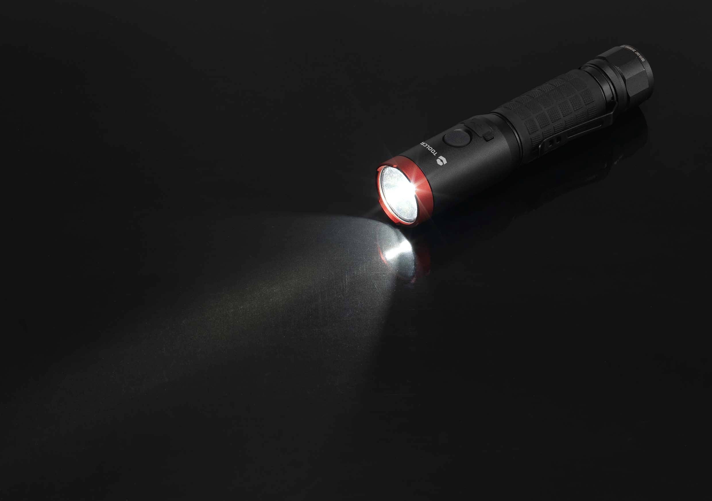 Eine schwarze Taschenlampe liegt auf einer dunklen Oberfläche und leuchtet mit einem weißen Lichtstrahl nach links.
