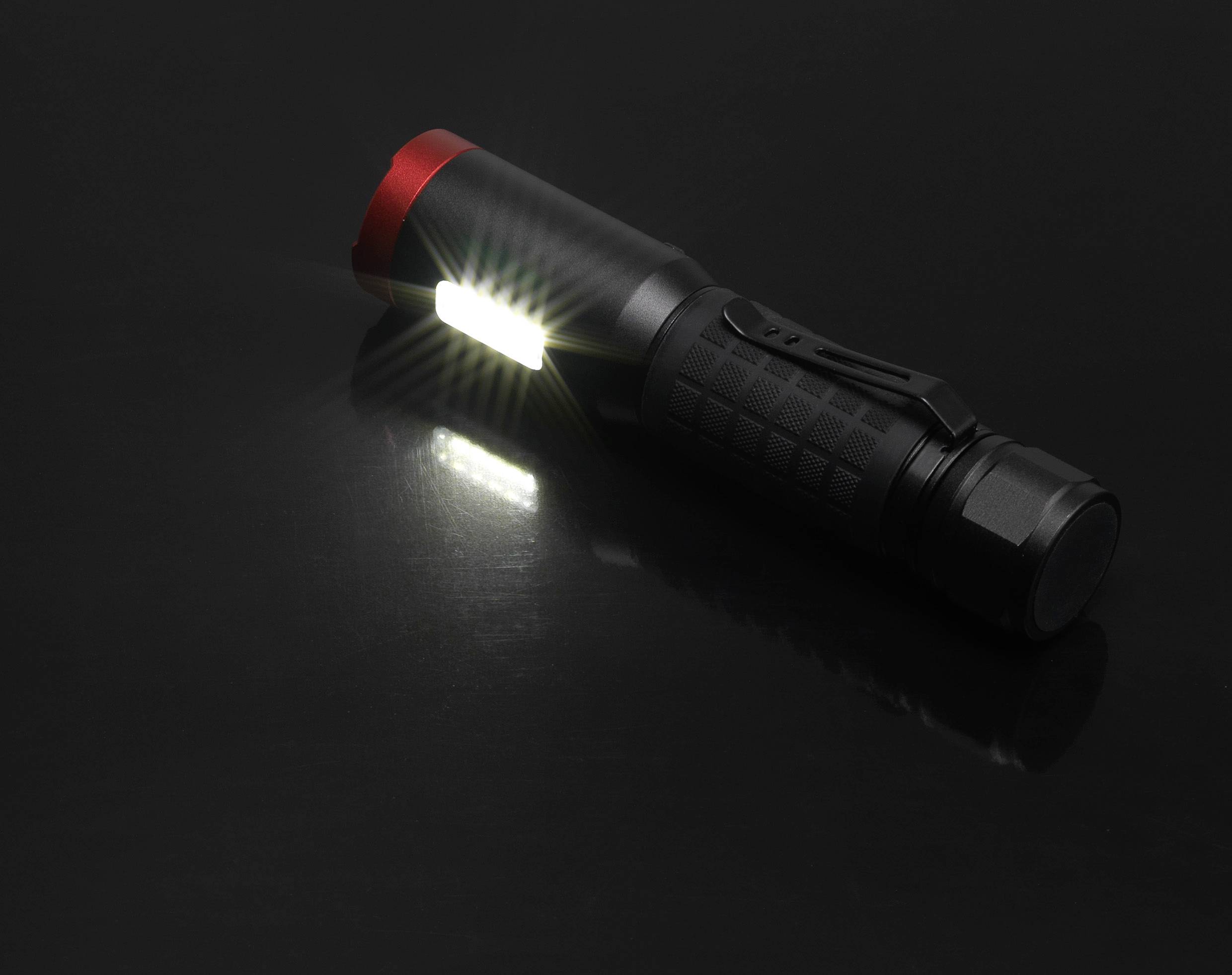 Eine schwarze Taschenlampe liegt auf einem dunklen Hintergrund und leuchtet helles Licht aus der Seite.