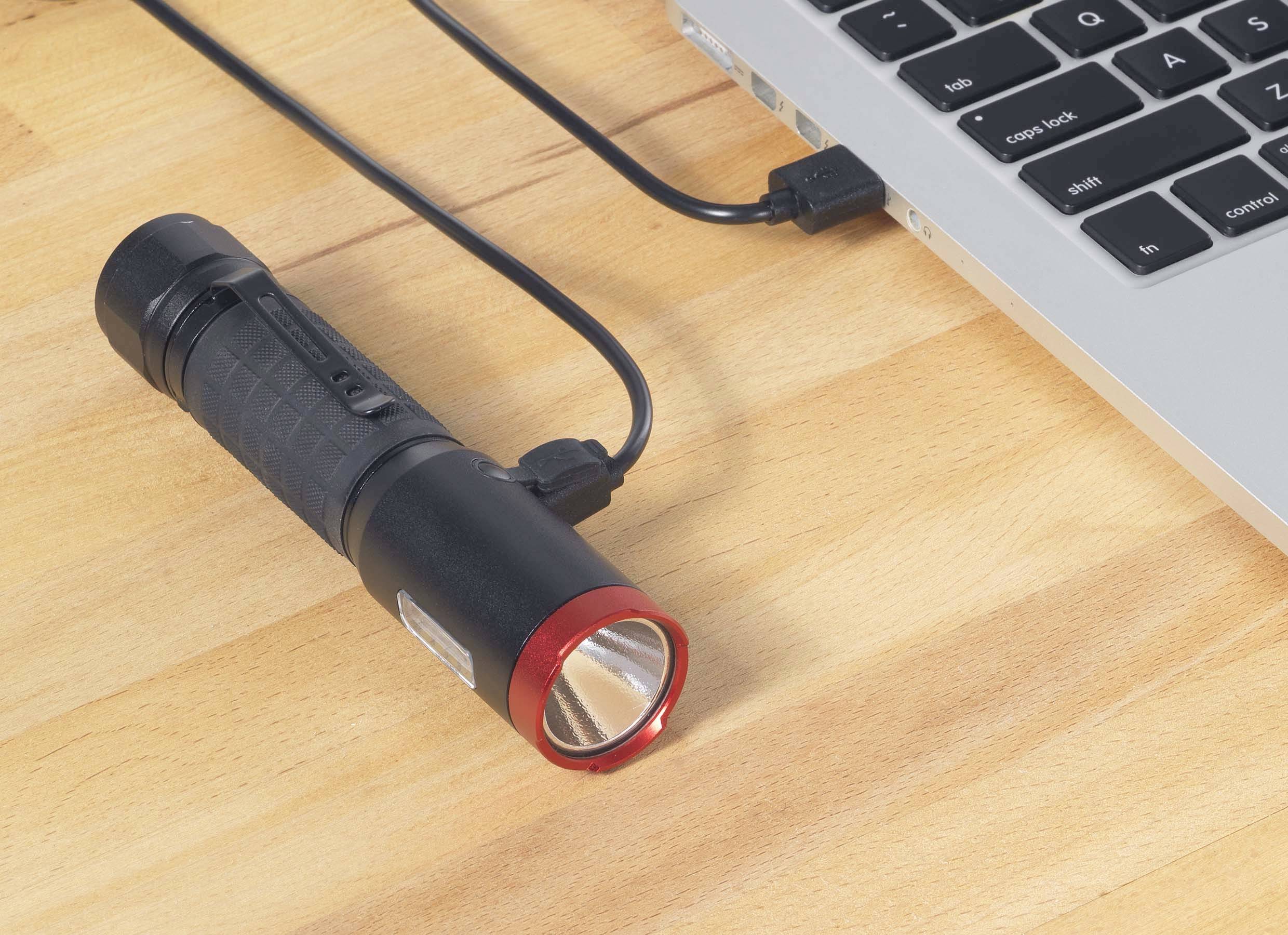 Taschenlampe mit rotem Rand lädt mit einem USB-Kabel verbunden an einem Laptop auf.