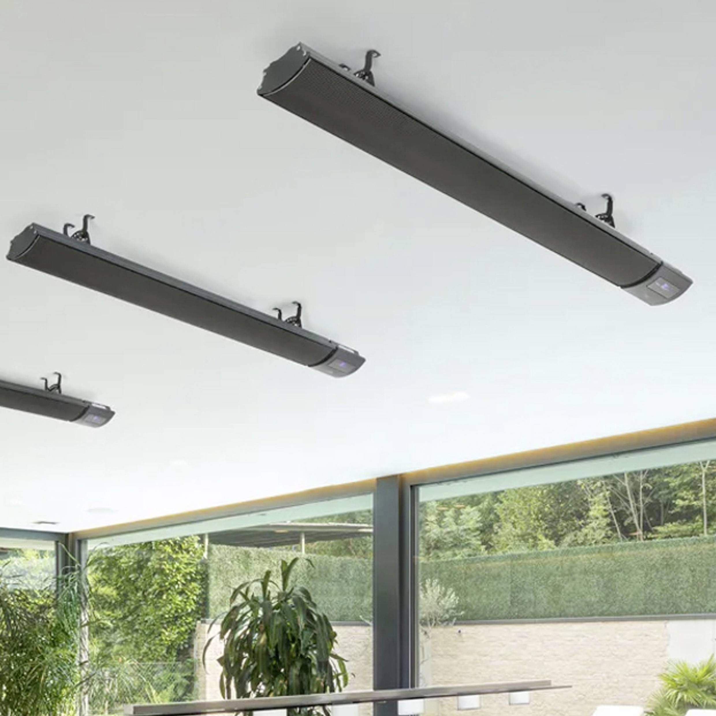 Mehrere schwarze Heizstrahler sind an der Decke einer modernen Terrasse angebracht, im Hintergrund sind grüne Pflanzen sichtbar.