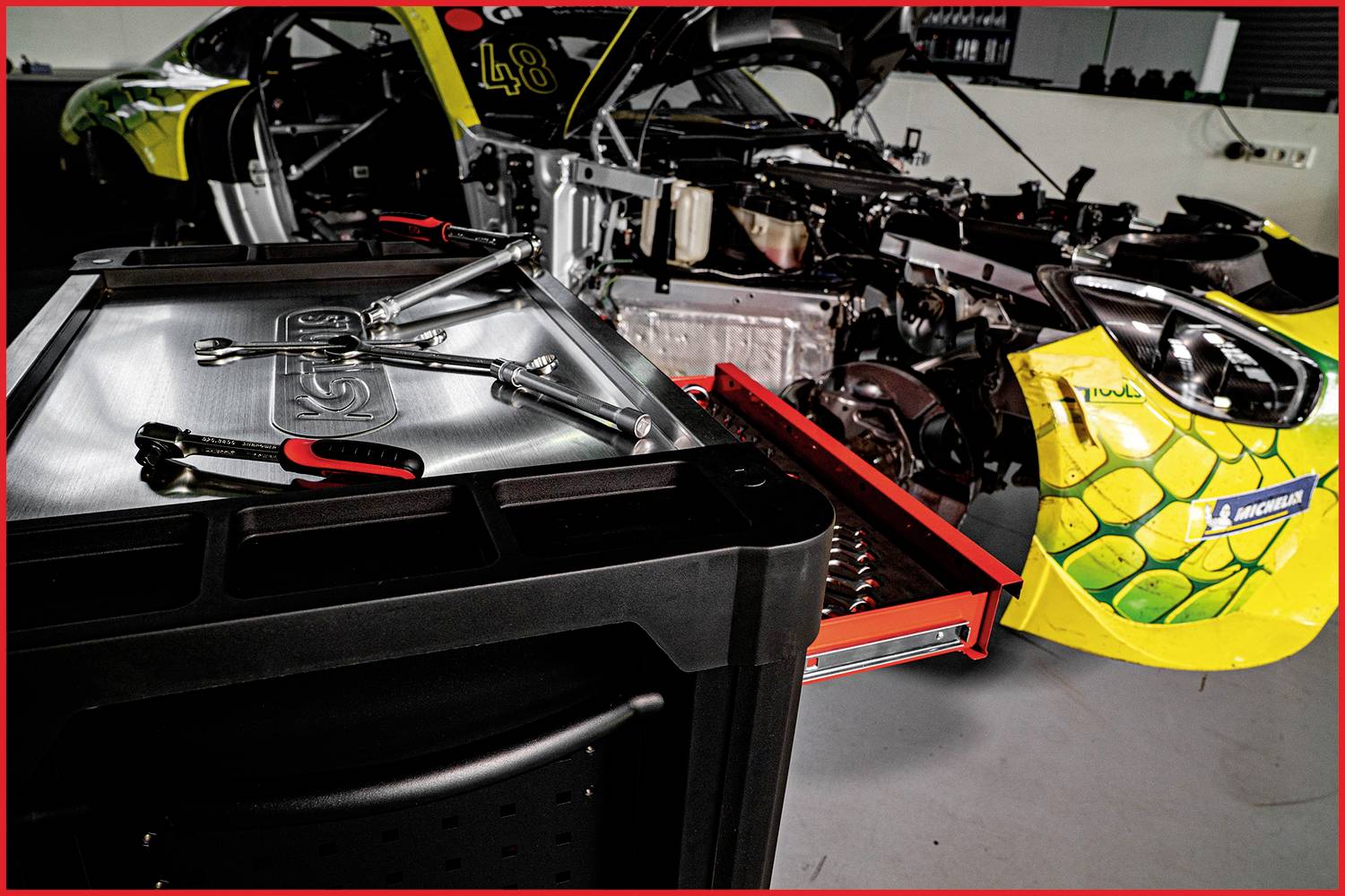Ein repariertes Rennauto in einer Werkstatt, mit offenem Motorraum. Werkzeug liegt auf einem Tisch im Vordergrund.
