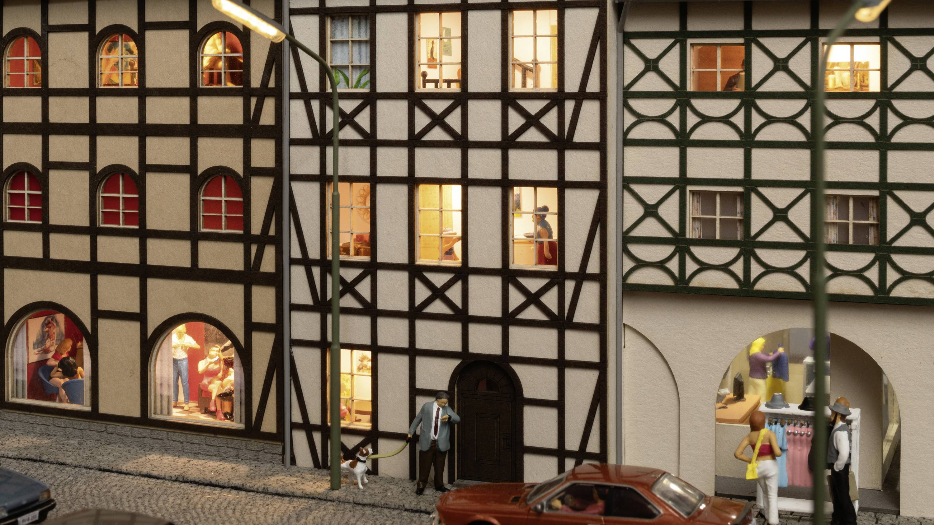 Modell einer Altstadtstraße mit Fachwerkhäusern, beleuchteten Fenstern und kleinen Figuren. Autos sind entlang der gepflasterten Straße geparkt.