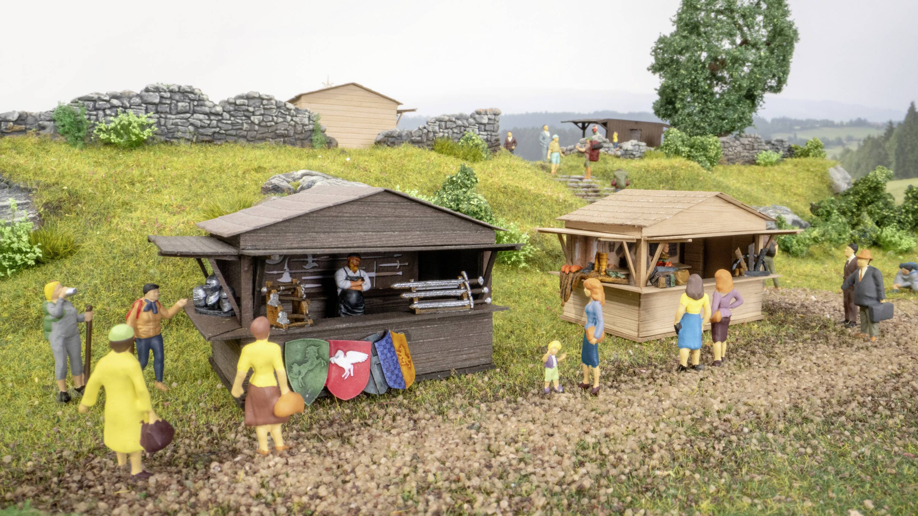 Ein belebter Marktplatz mit Ständen und Menschen in bunter Kleidung, umgeben von grünen Wiesen und Bäumen, unter einem bewölkten Himmel.