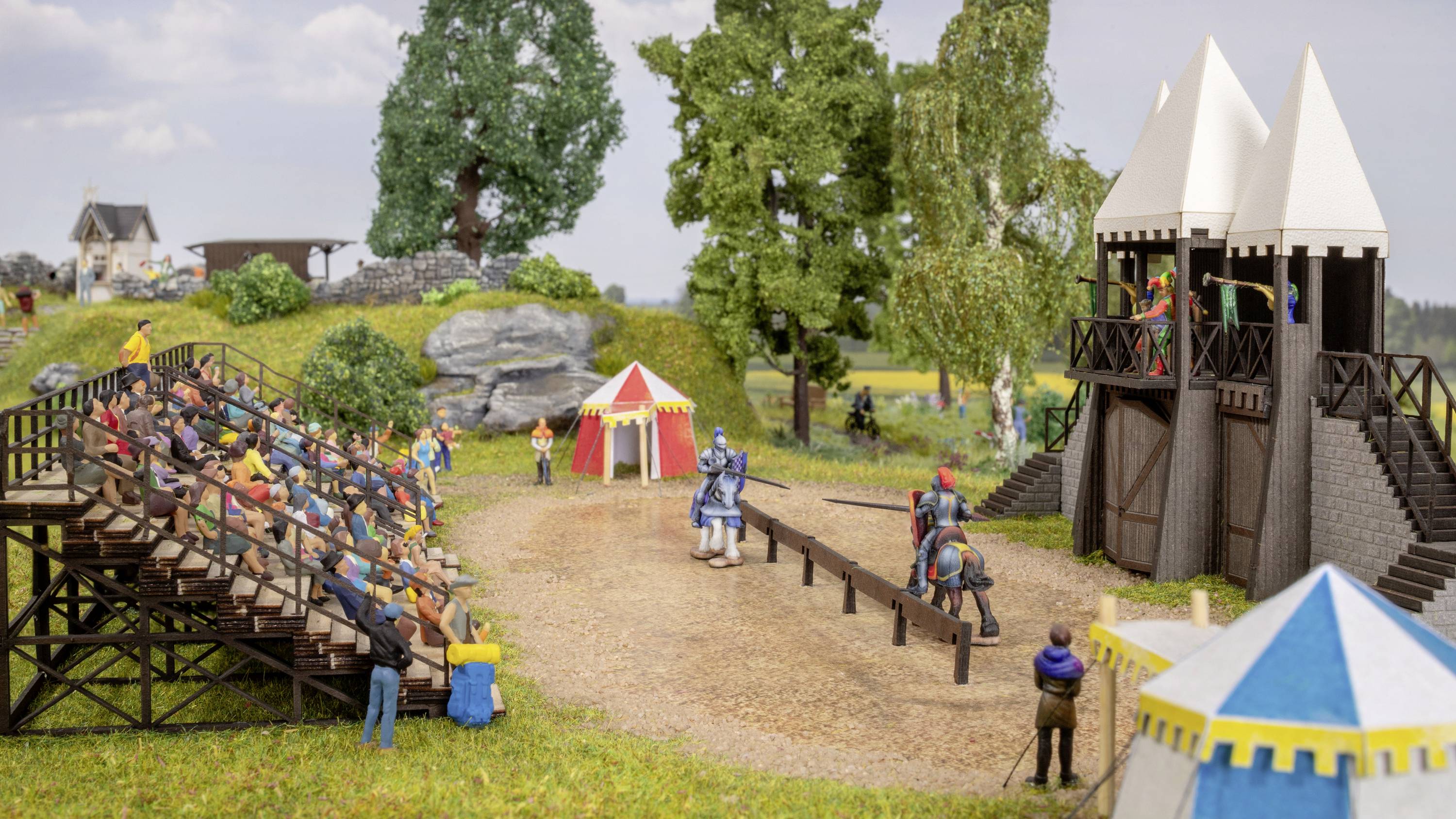 Ritterturnier-Szene in Miniatur: Zwei Ritter zu Pferd kämpfen auf einer Sandarena, umgeben von Publikum auf Tribünen und Zelten.