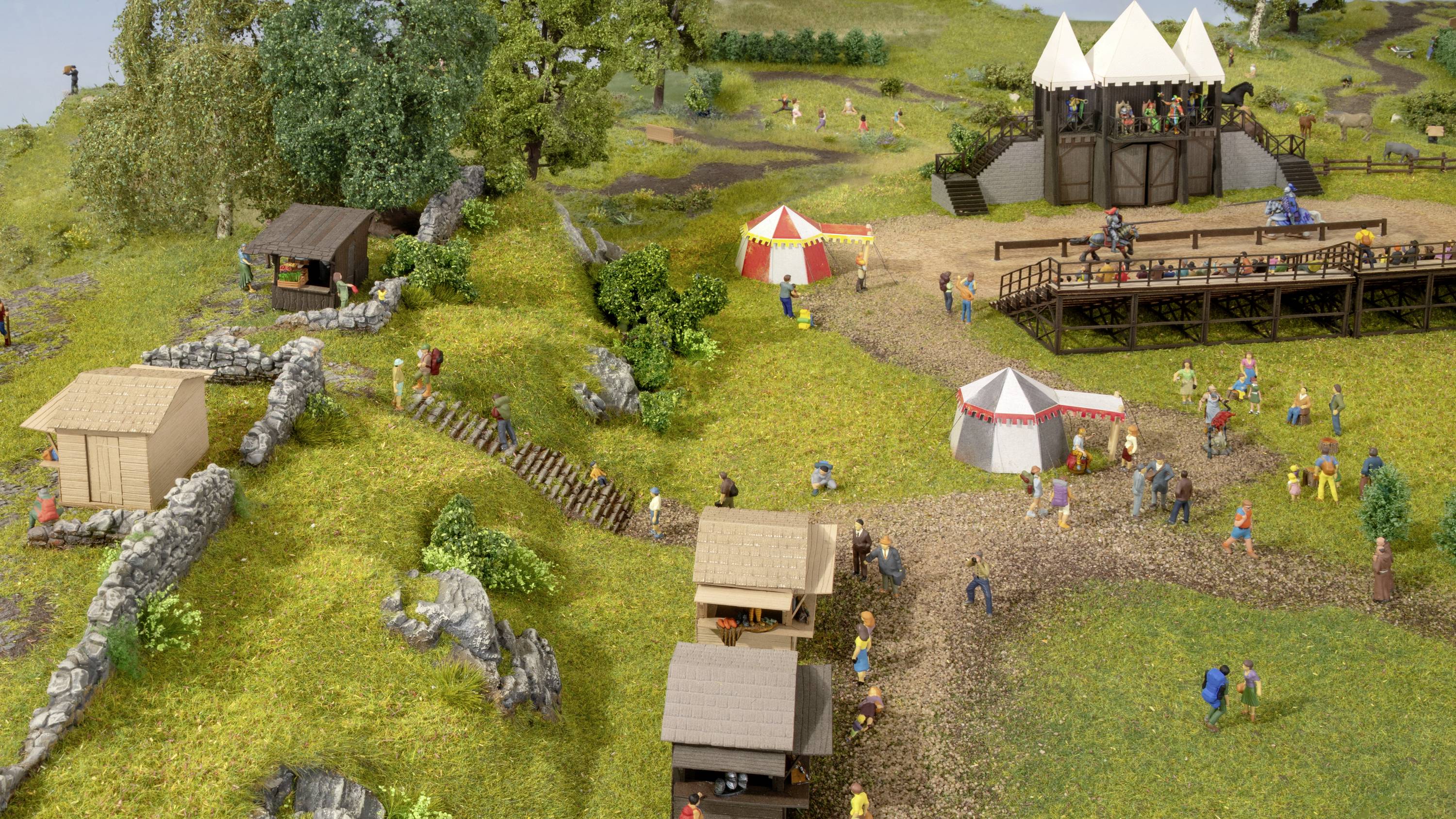 Miniaturmodell eines Mittelaltermarkts mit Zelten, Holzständen und Figuren in mittelalterlicher Kleidung auf einer grünen Wiese.