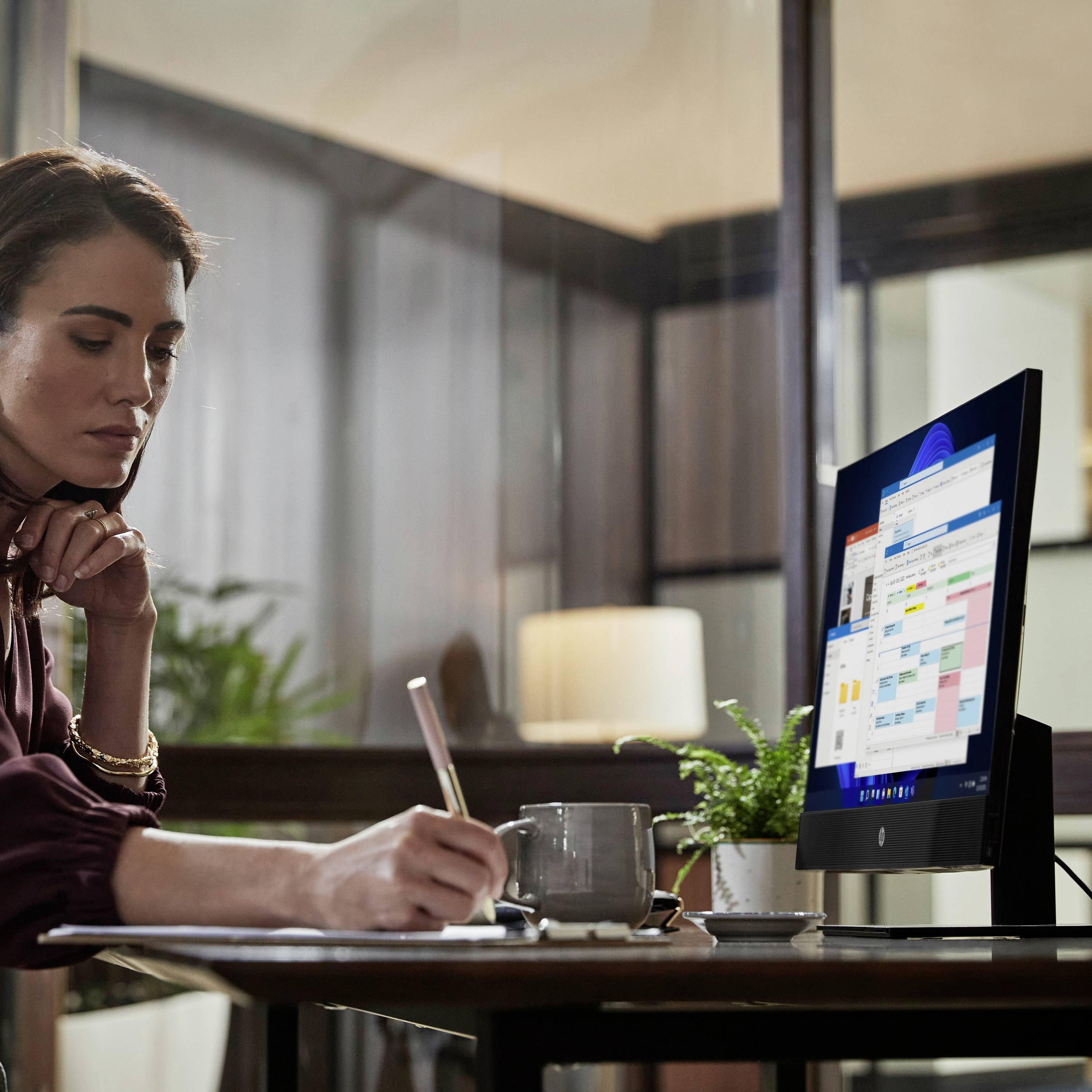 Eine Frau arbeitet konzentriert an einem Computer in einem modernen Büro. Auf dem Schreibtisch stehen Pflanzen und Büroartikel.