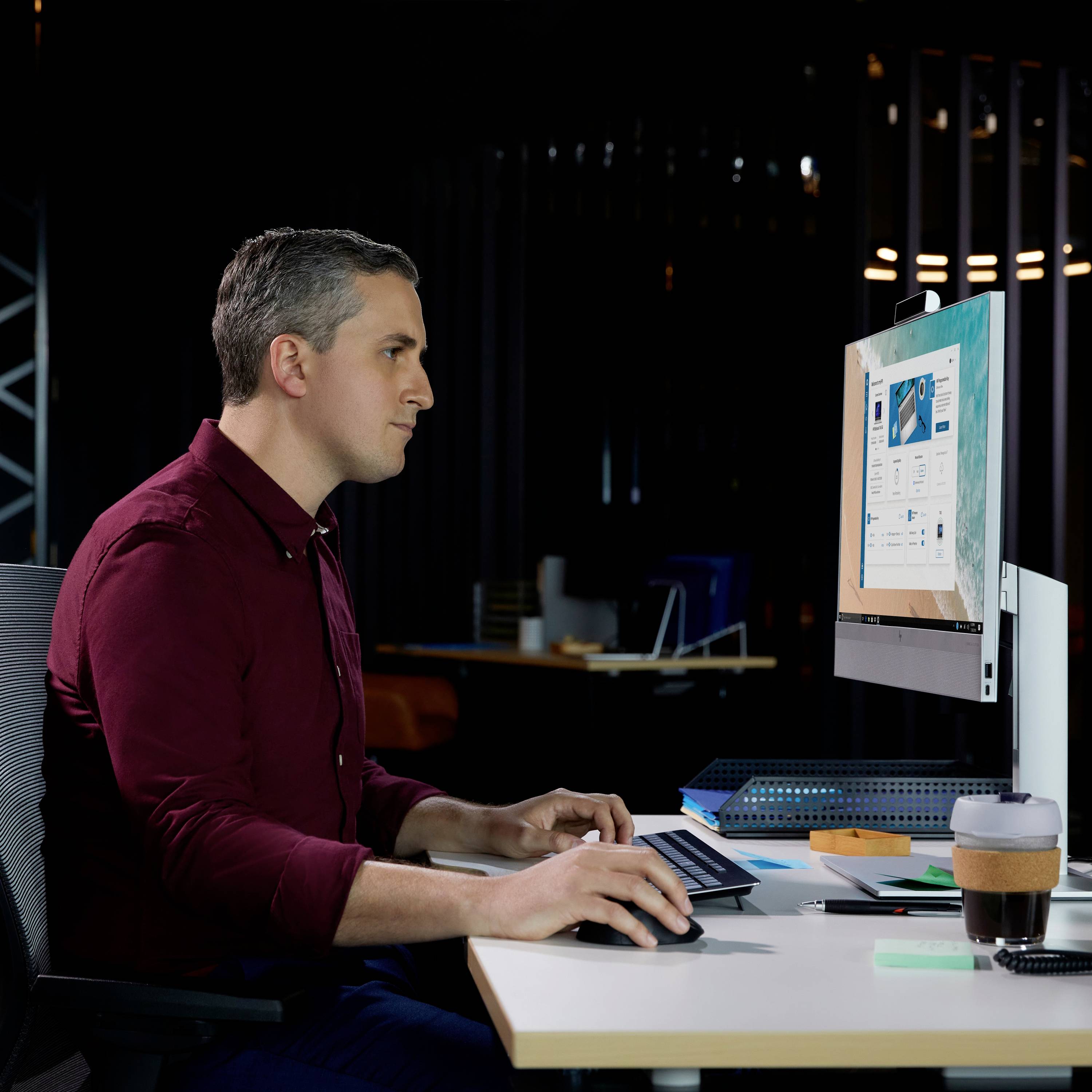 Ein Mann sitzt am Schreibtisch, arbeitet am Computer in einem modernen Büro mit mehreren Monitoren und Bürobedarf auf dem Tisch.