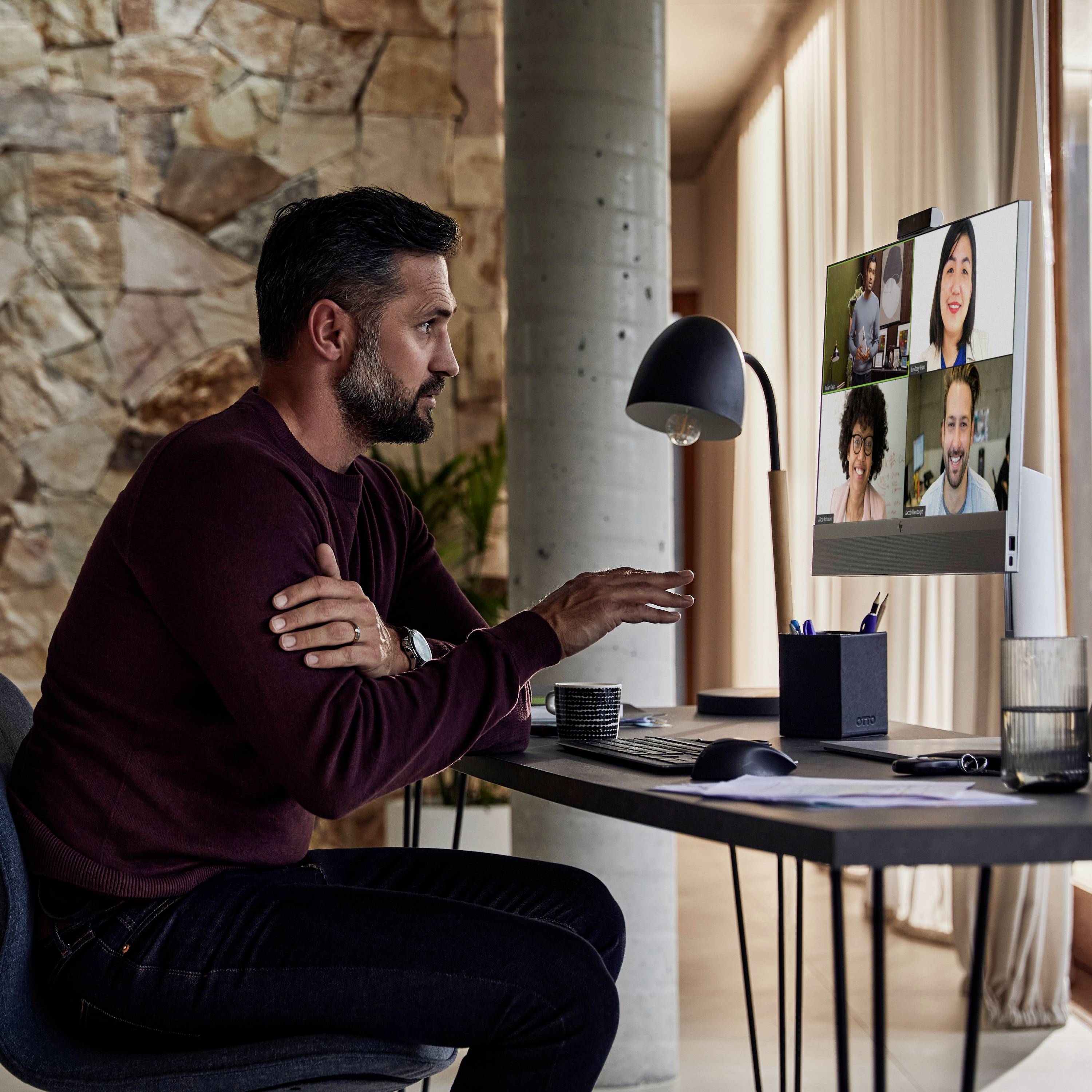 Ein Mann sitzt an einem Tisch und nimmt an einer Videokonferenz mit vier weiteren Personen auf einem Computerbildschirm teil.
