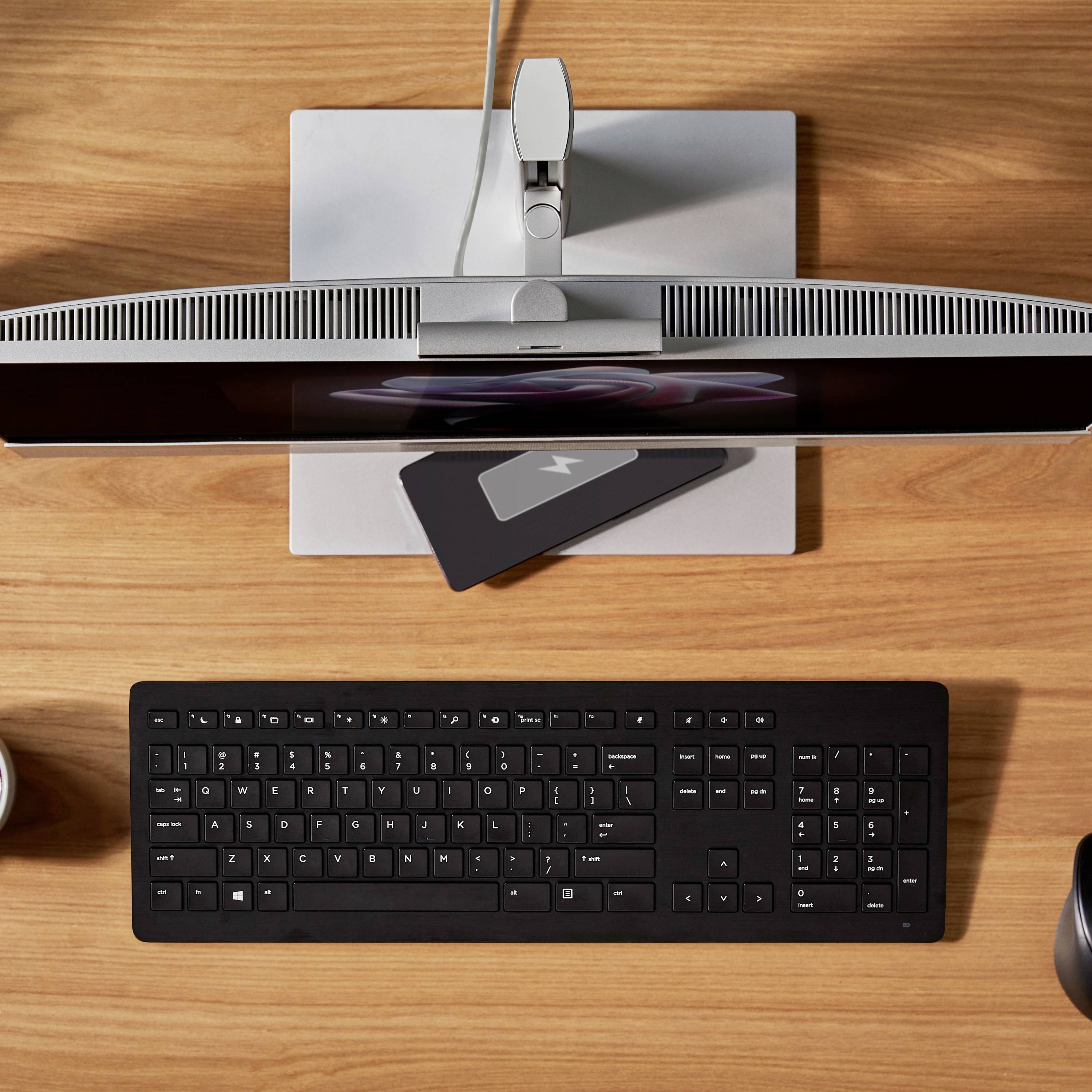 Ein Schreibtisch mit einem Monitor, einer schwarzen Tastatur und einem Laptop. Kabel verbinden die Geräte. Alles ist ordentlich arrangiert.