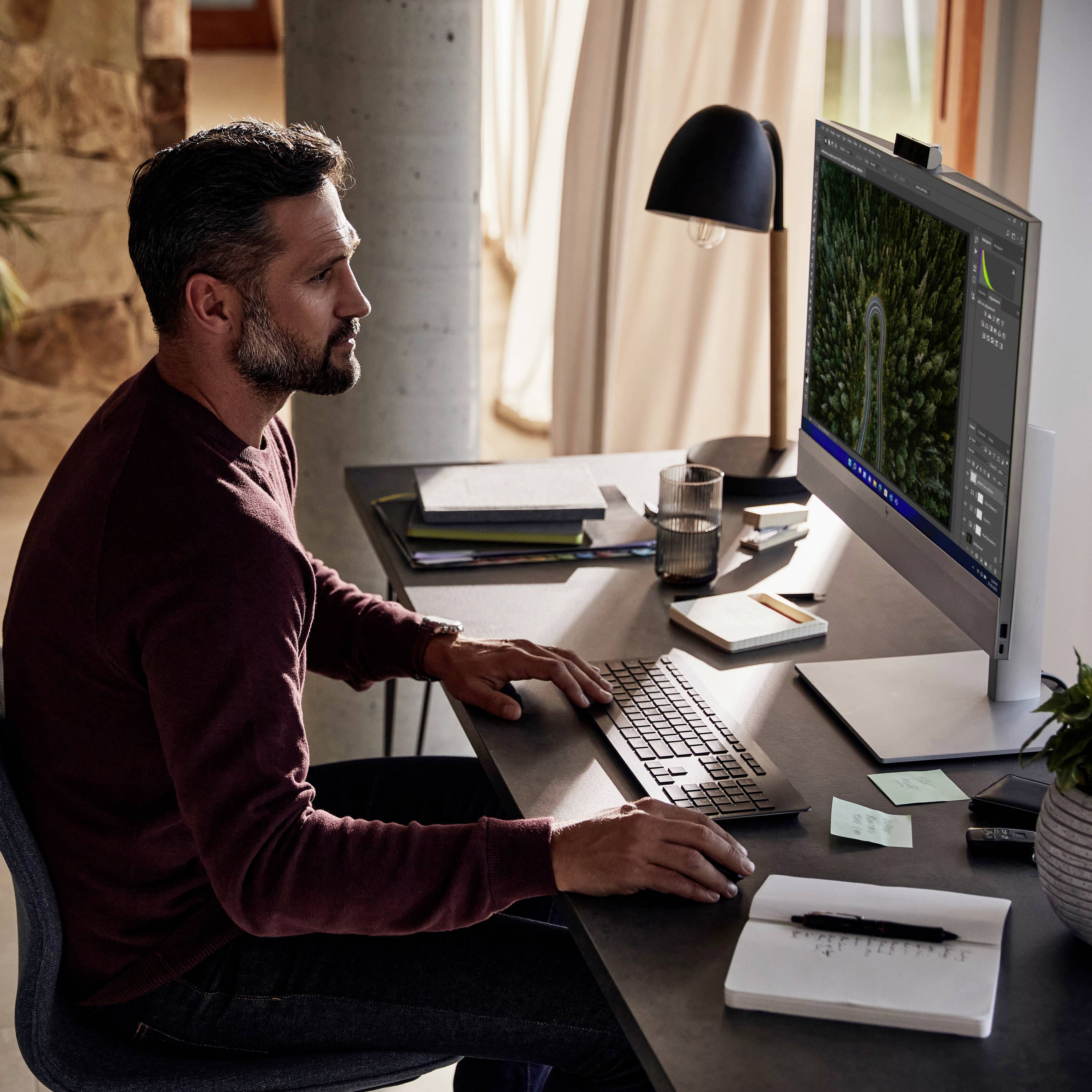 Ein Mann arbeitet an einem Schreibtisch mit einem Computerbildschirm. Der Raum ist hell, und es sind Büro- und Schreibmaterialien zu sehen.