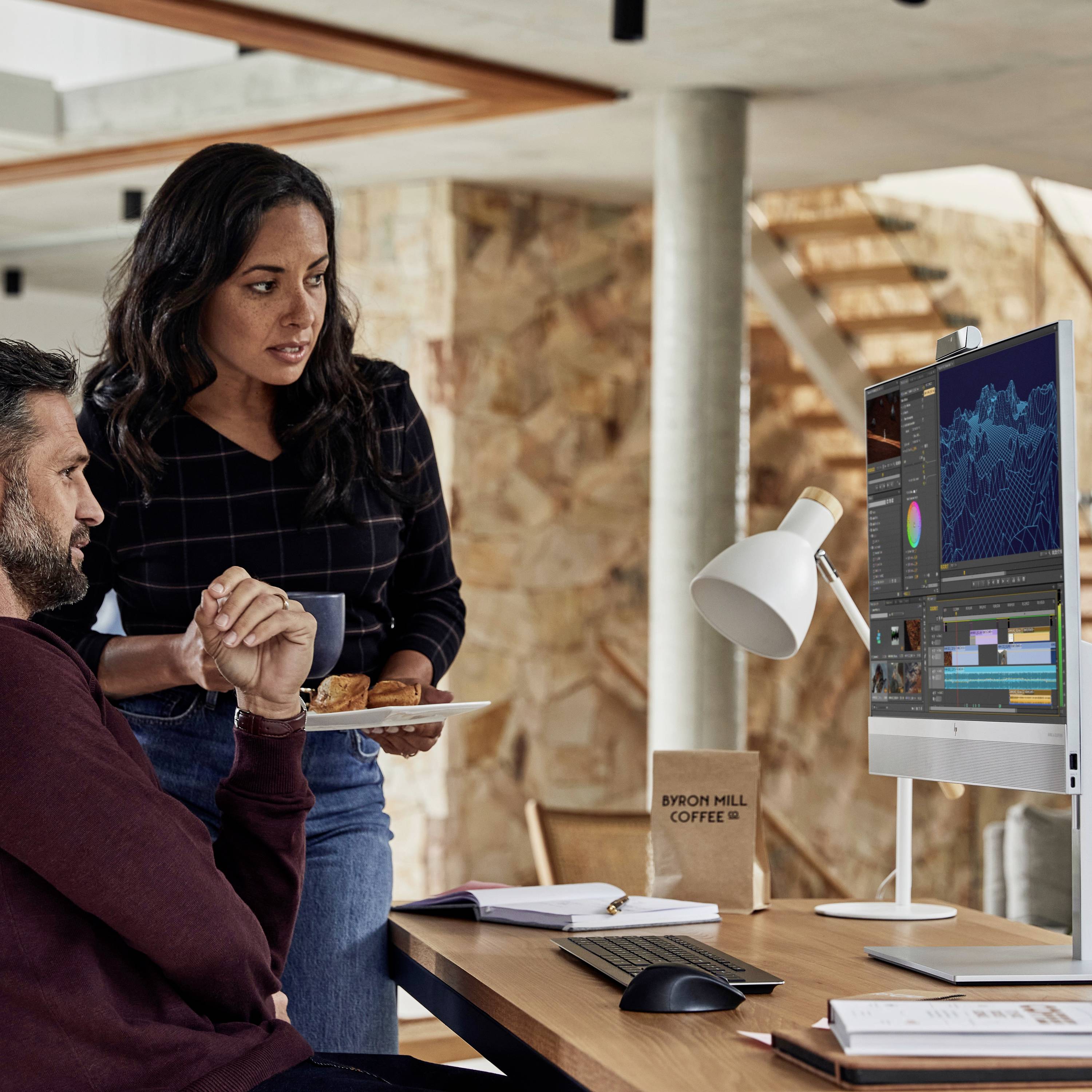 Mann und Frau in einem Büro, betrachten einen Computerbildschirm mit Diagrammen und Grafiken. Tisch mit Laptop, Kaffee, und Notizblock.