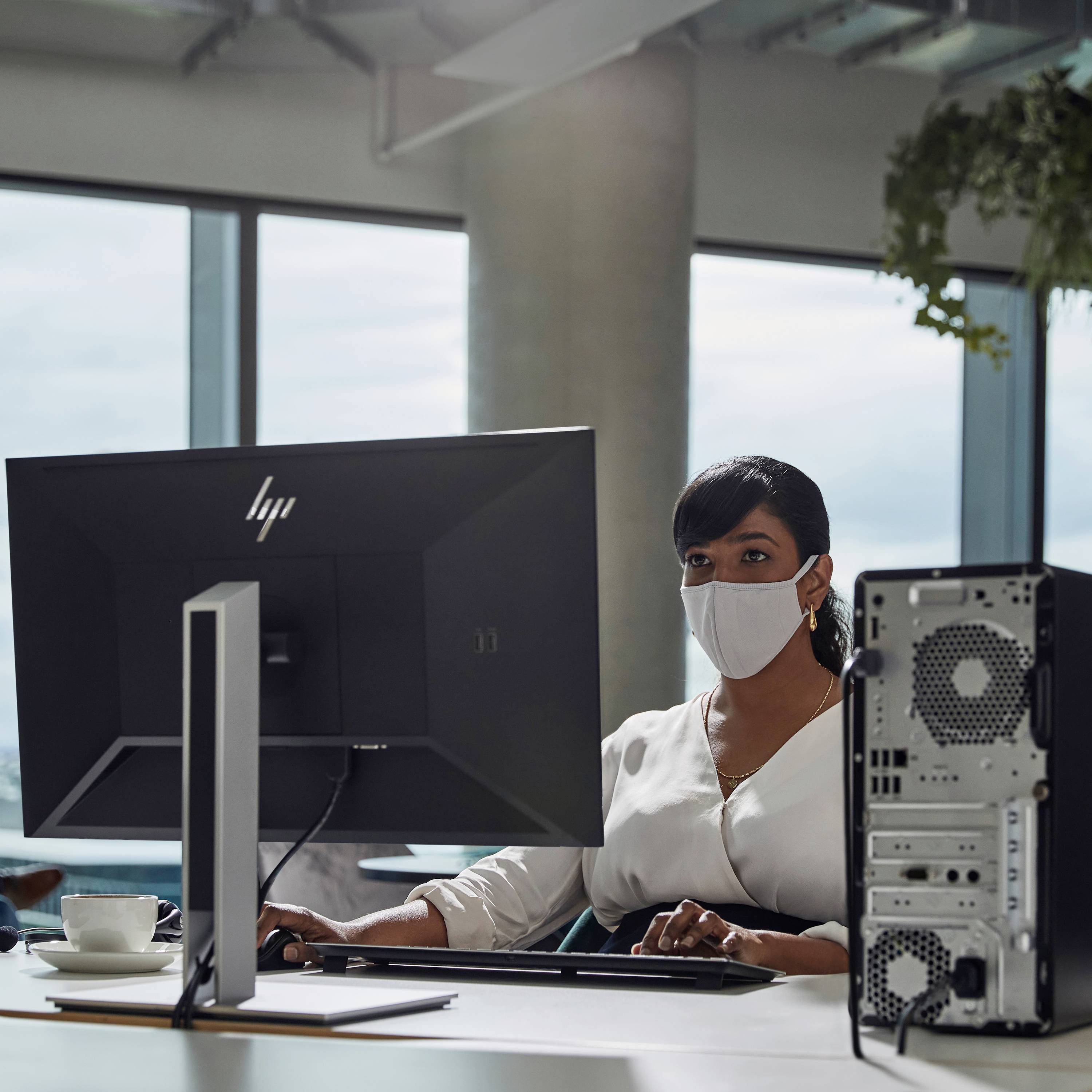 Eine Person sitzt am Schreibtisch vor einem Computer und spricht in ein Headset. Die Umgebung wirkt modern und hell beleuchtet.