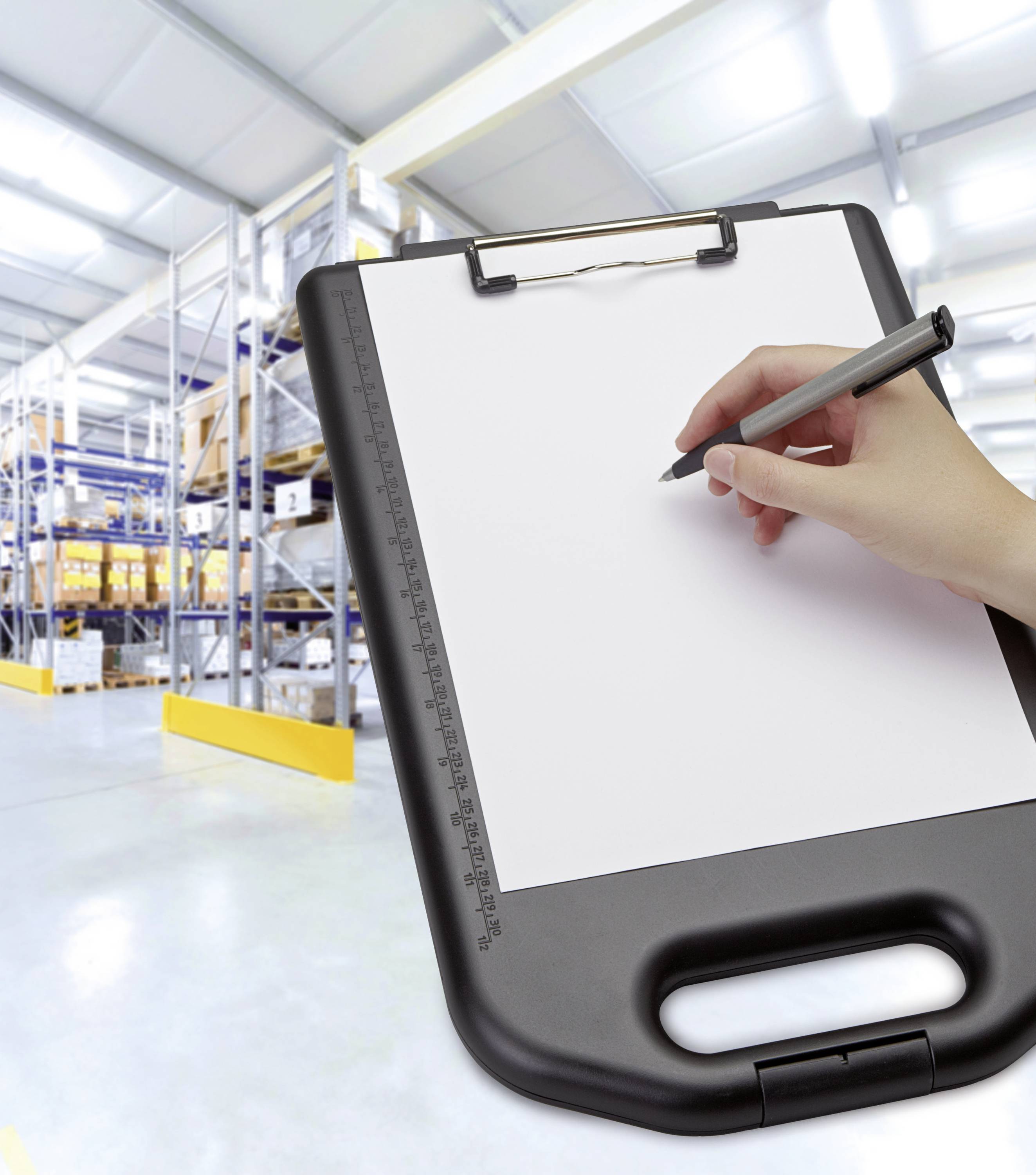 Eine Hand schreibt mit einem Stift auf ein Klemmbrett vor einem Lager mit Regalen voller Kartons.