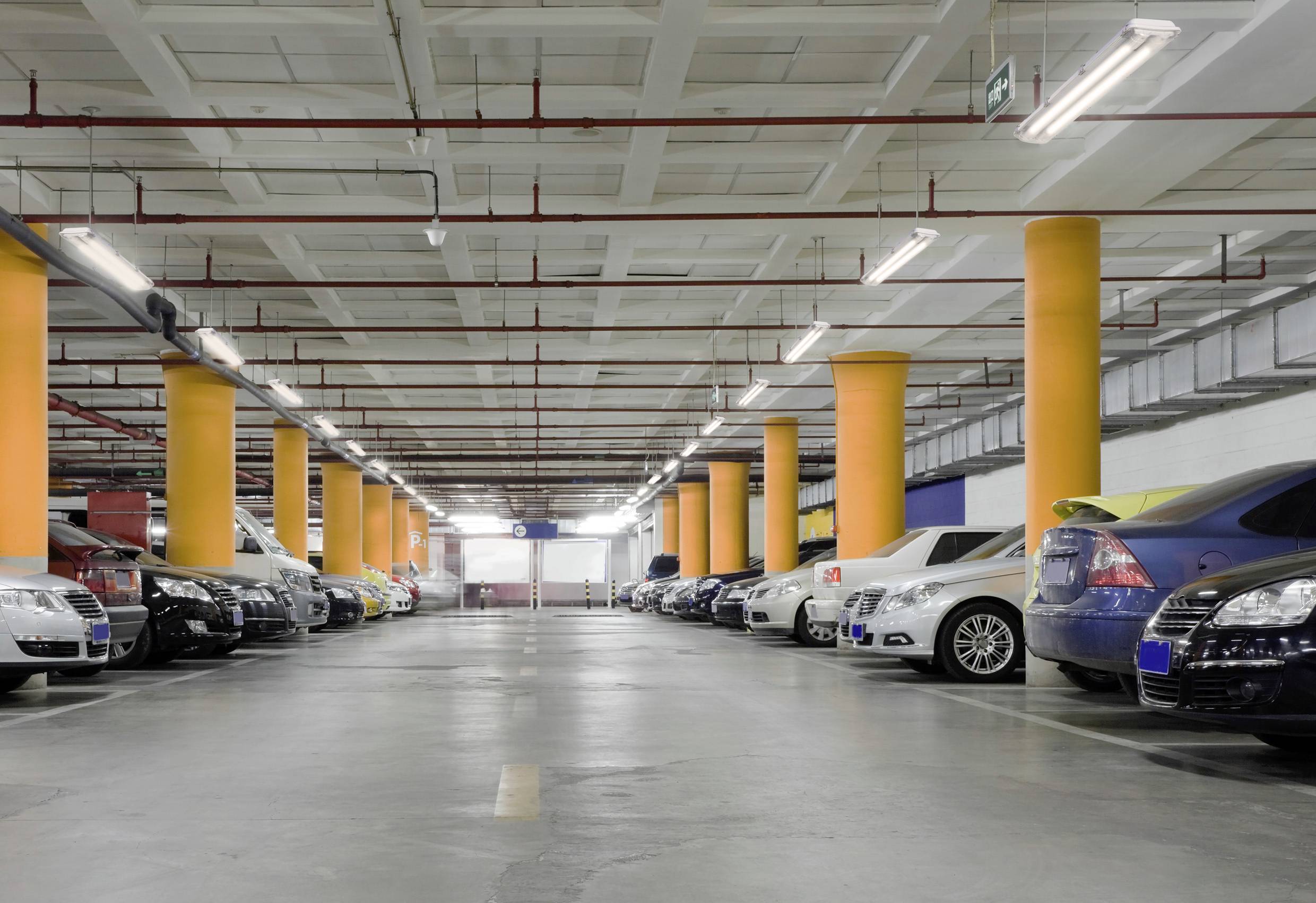 Eine Tiefgarage mit geparkten Autos auf beiden Seiten. Helle Beleuchtung und gelbe Säulen sind zu sehen.