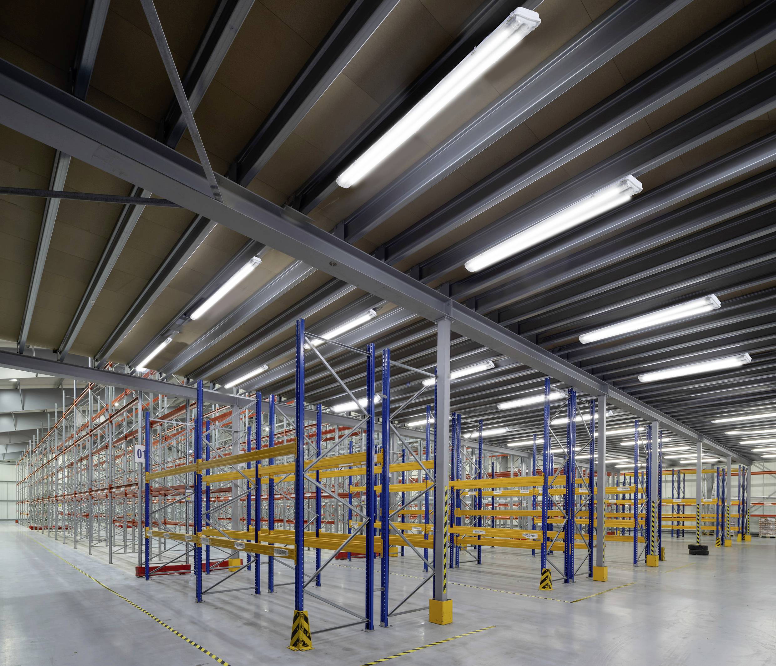 Leeres Lagerhaus mit hohen Regalen; keine Produkte gelagert; Beleuchtung von LED-Leuchten an der Decke; gelber Sicherheitsmarkierung am Boden.