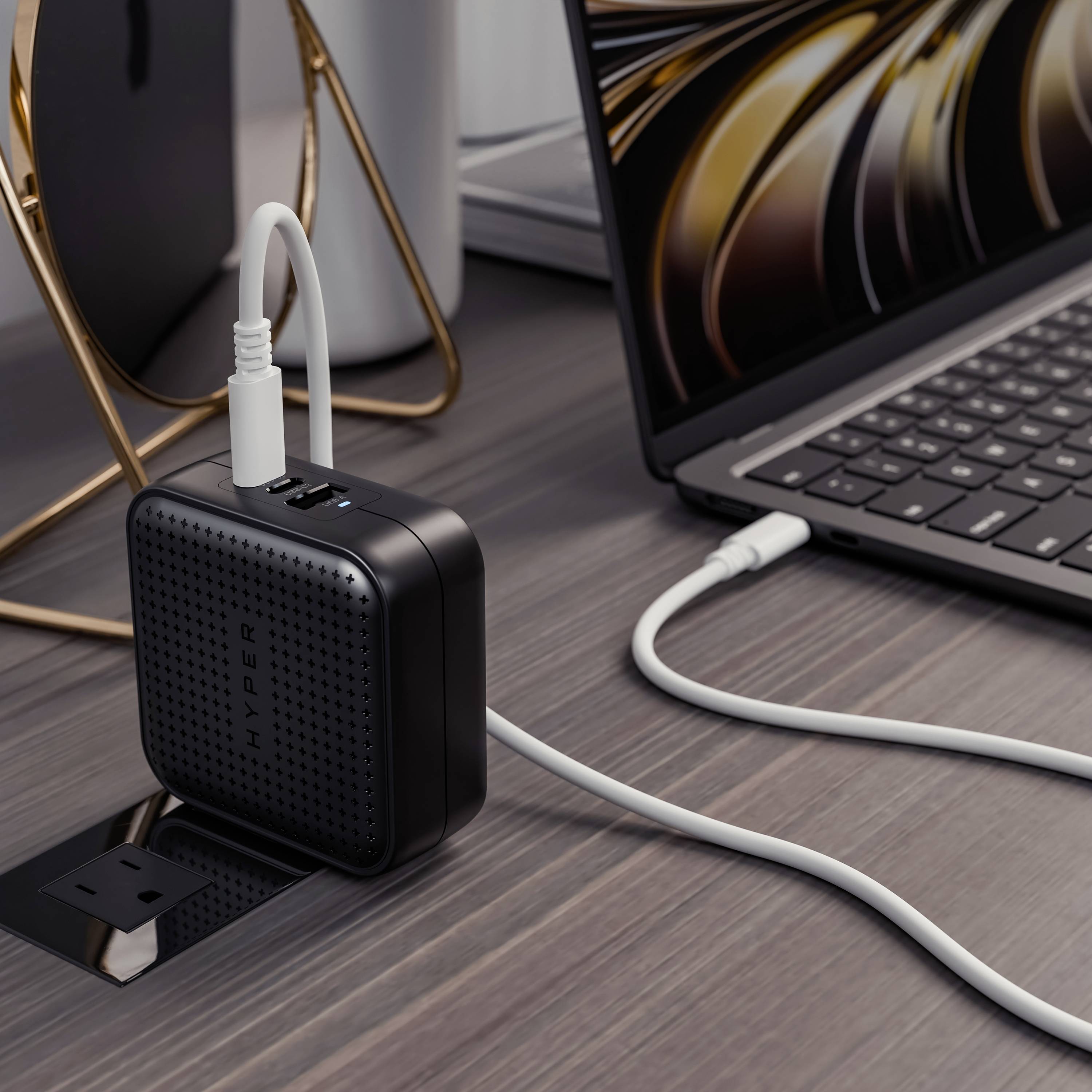 Ein Laptop ist an eine Mehrfachsteckdose mit USB-Anschlüssen angeschlossen, die auf einem Tisch neben einem Smartphone steht.