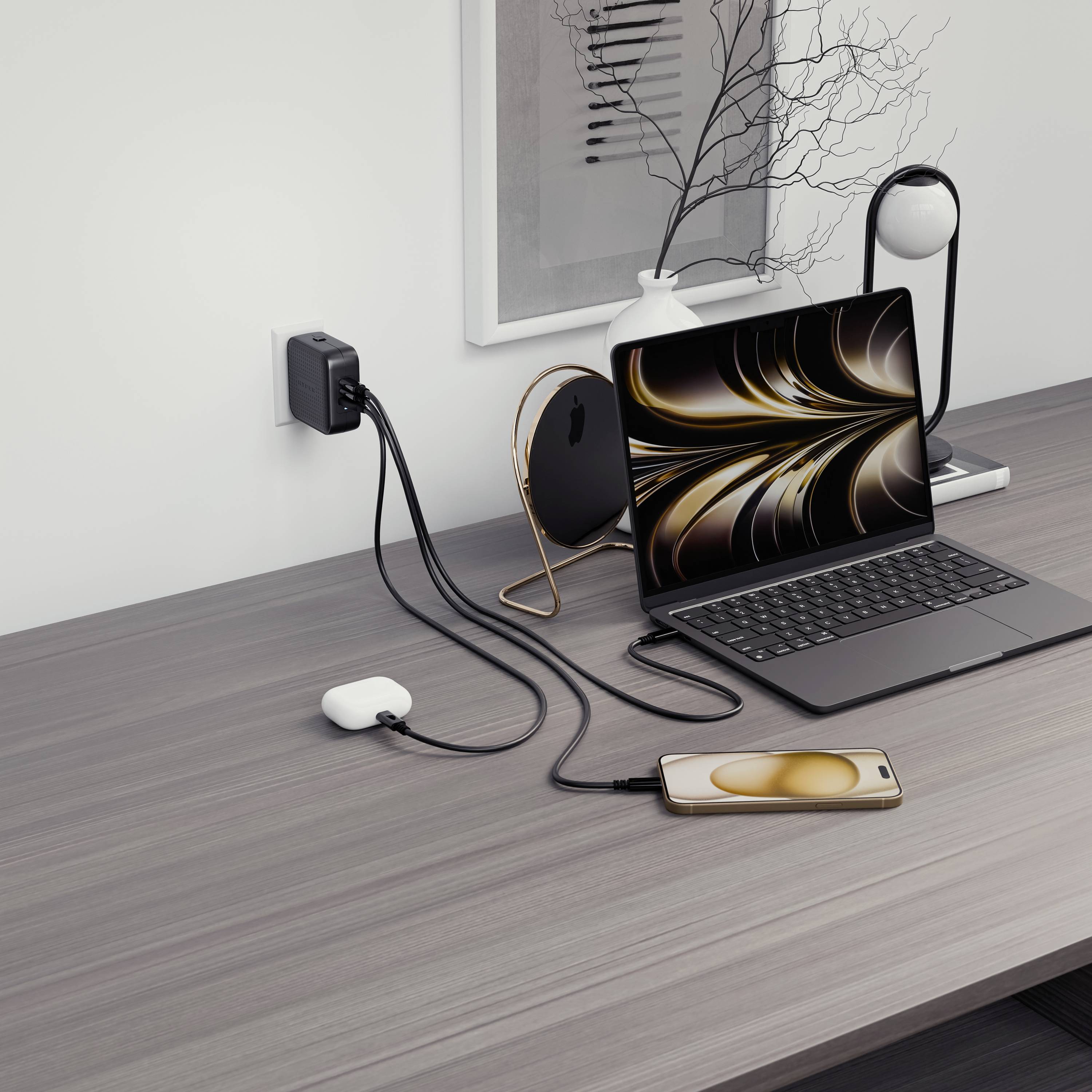Ein Schreibtisch mit einem Laptop, einem Smartphone und Ladekabeln; der Laptop ist an das Smartphone angeschlossen; modernes Ladegerät in der Steckdose.
