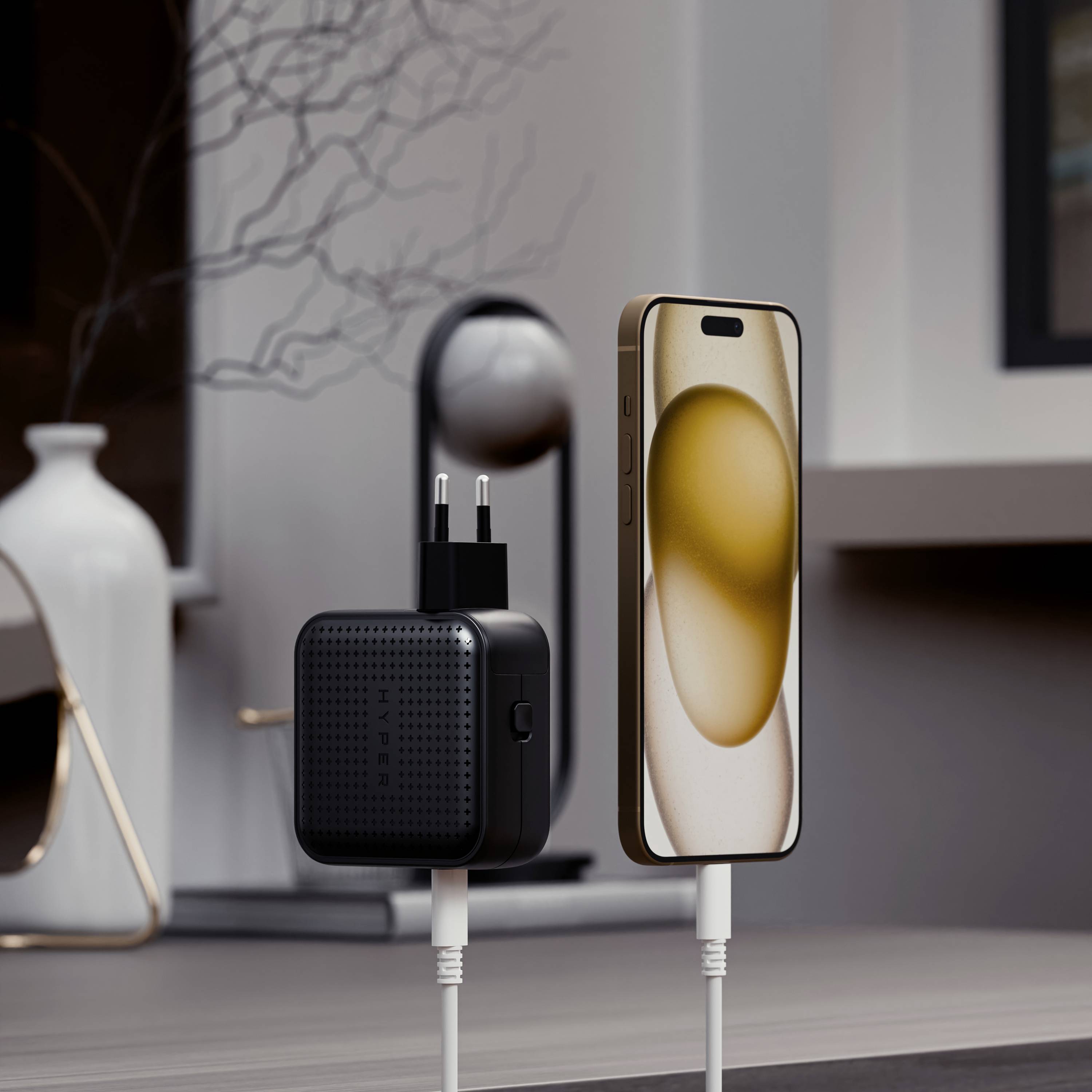 Ein Smartphone wird kabellos aufgeladen. Ein Ladegerät steht daneben, angeschlossen an eine Steckdose. Im Hintergrund ist modernes Dekor.