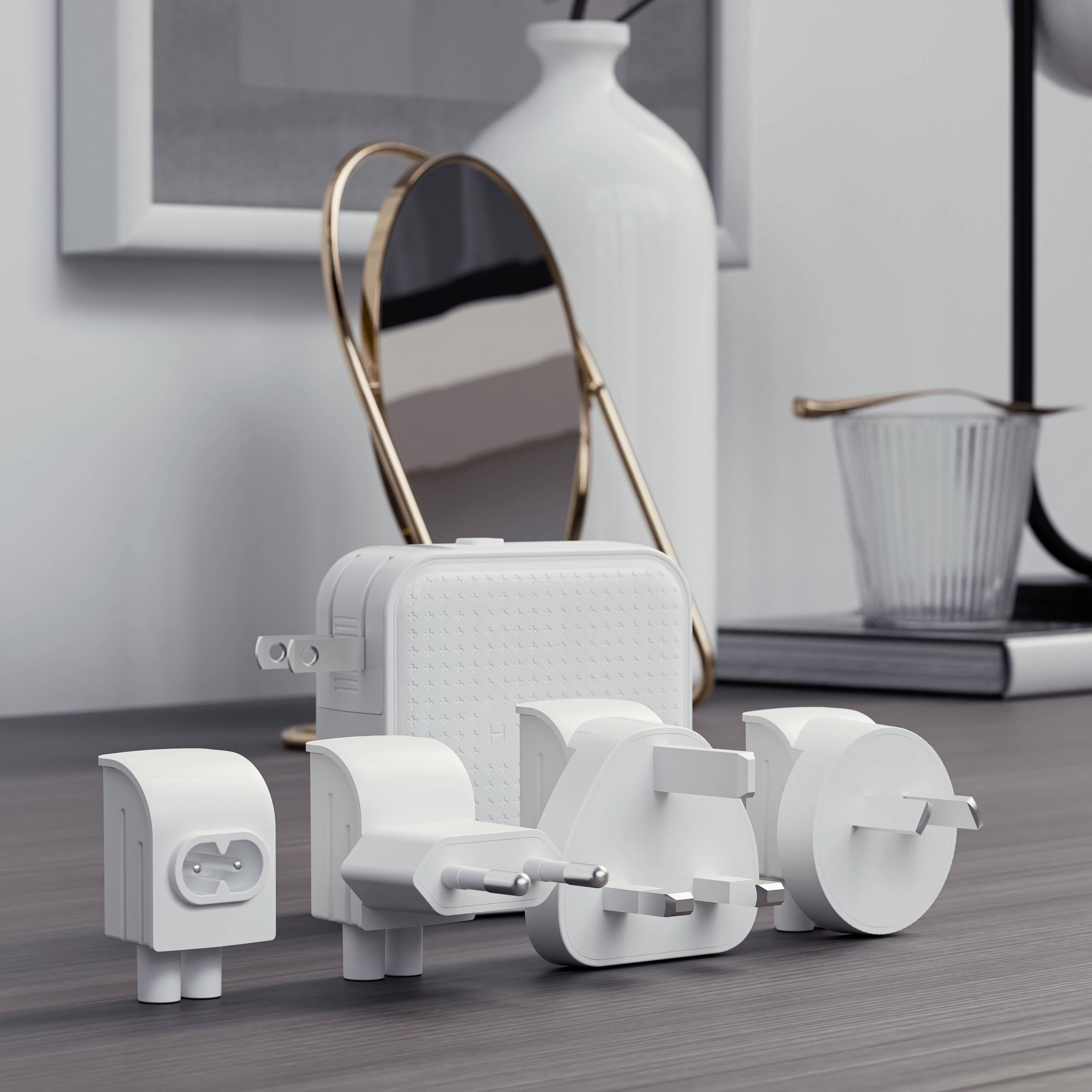 Mehrere internationale Steckdosenadapter auf einem Tisch, mit einer Vase, einem Spiegel, und einem Buch im Hintergrund.
