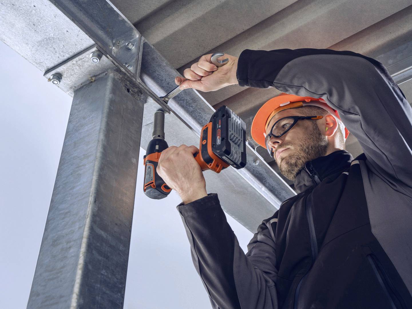 Ein Bauarbeiter mit Schutzhelm verwendet einen Akkuschrauber, um ein Metalltreppengeländer zu befestigen.