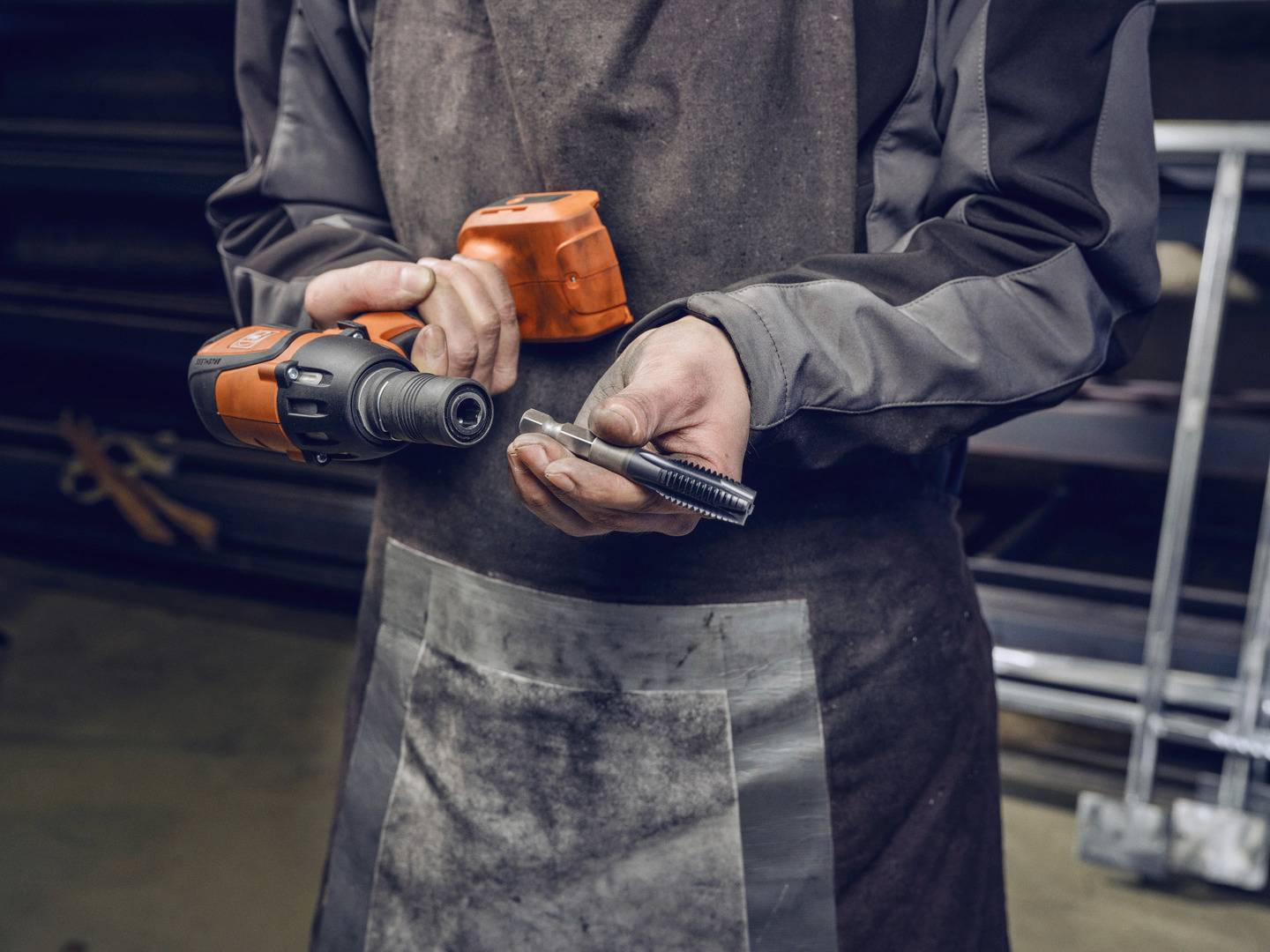 Eine Person in Arbeitskleidung hält eine elektrische Bohrmaschine in der rechten Hand und eine Schraube in der linken Hand.