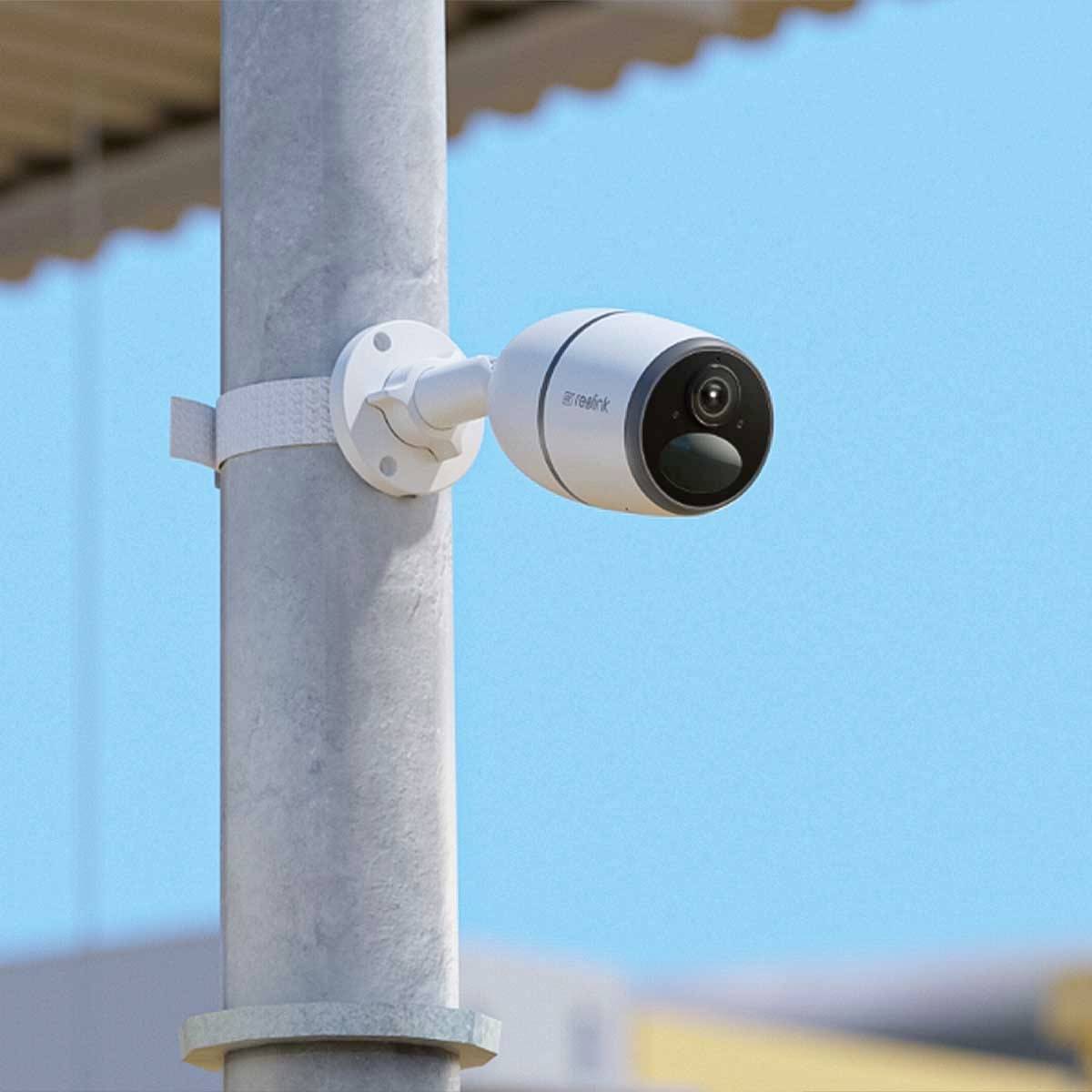 Überwachungskamera an einem Mast montiert, zeigt nach rechts. Heller, klarer Himmel im Hintergrund.