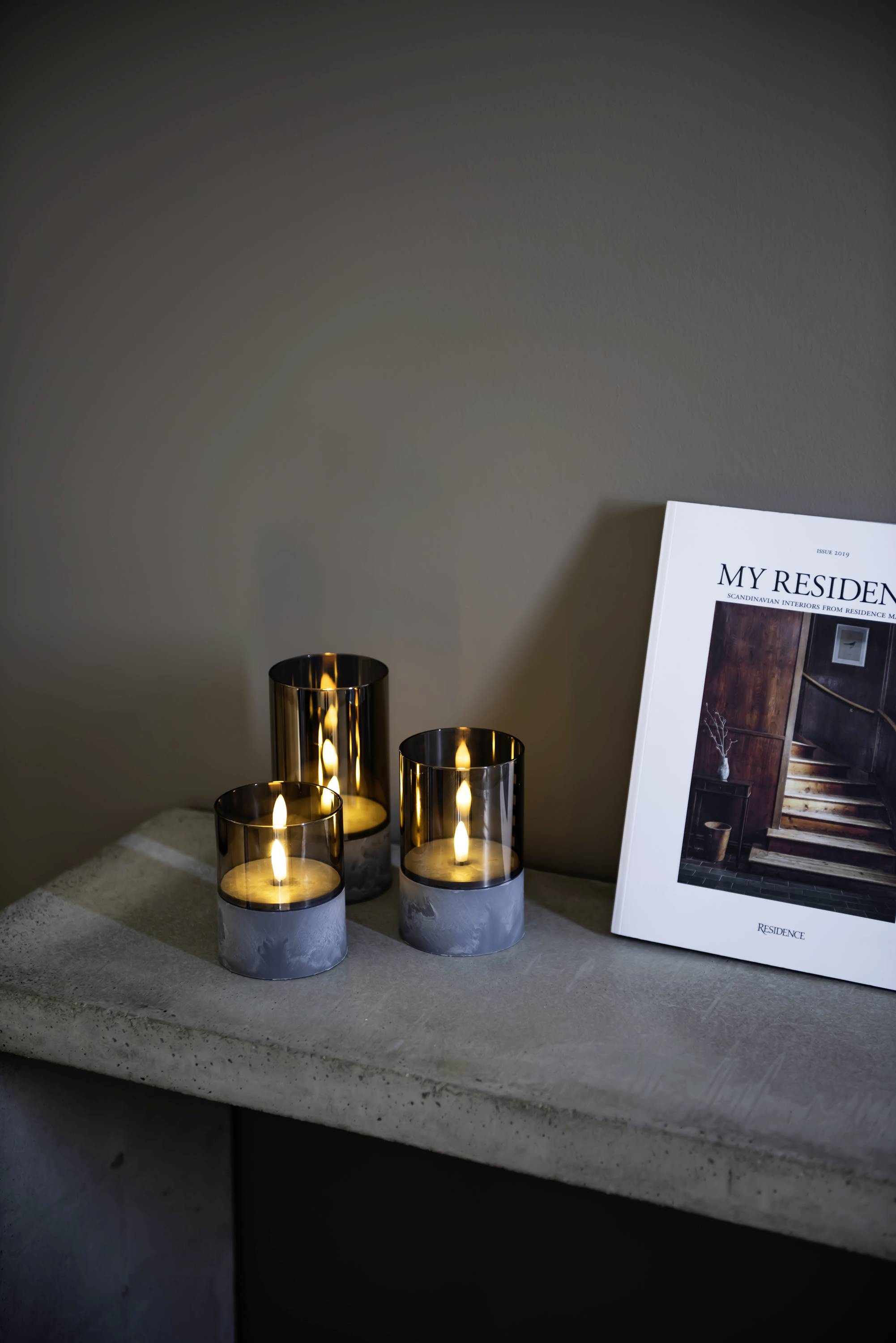 Drei brennende Kerzen stehen auf einem Tisch neben einem Magazin mit dem Titel 'My Residence', das eine Treppe auf dem Cover zeigt.