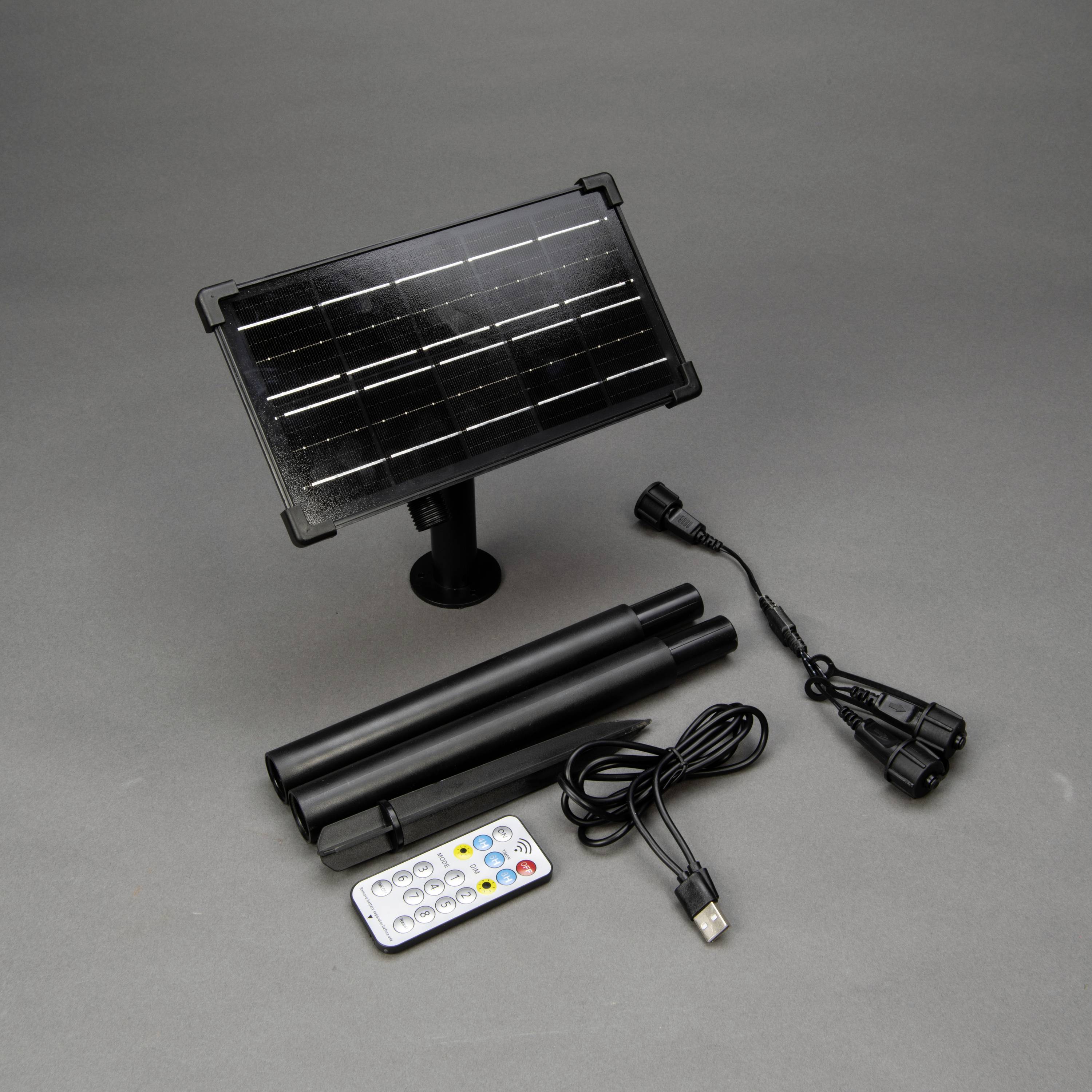 Solarladegerät mit Solarpanel, zwei abnehmbare Stangen, USB-Kabel, Fernbedienung und Adapter auf grauem Hintergrund.