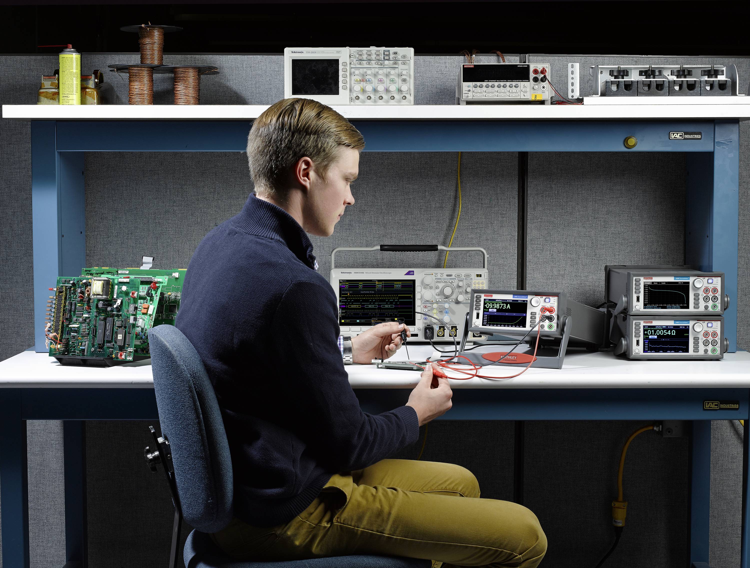 Eine Person arbeitet an einem Elektronik-Arbeitsplatz mit verschiedenen Messgeräten und einem offenen Schaltkreis.