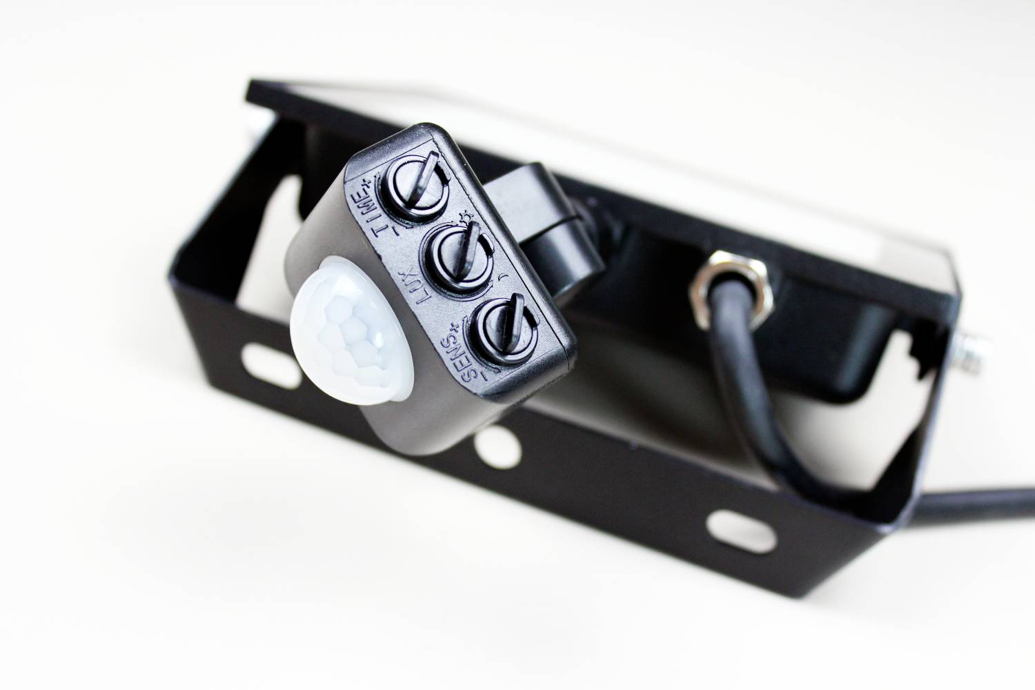 Ein schwarzer Bewegungssensor mit drei Drehknöpfen für 'Time', 'Lux' und 'SENS' ist an einer schwarzen Halterung montiert.