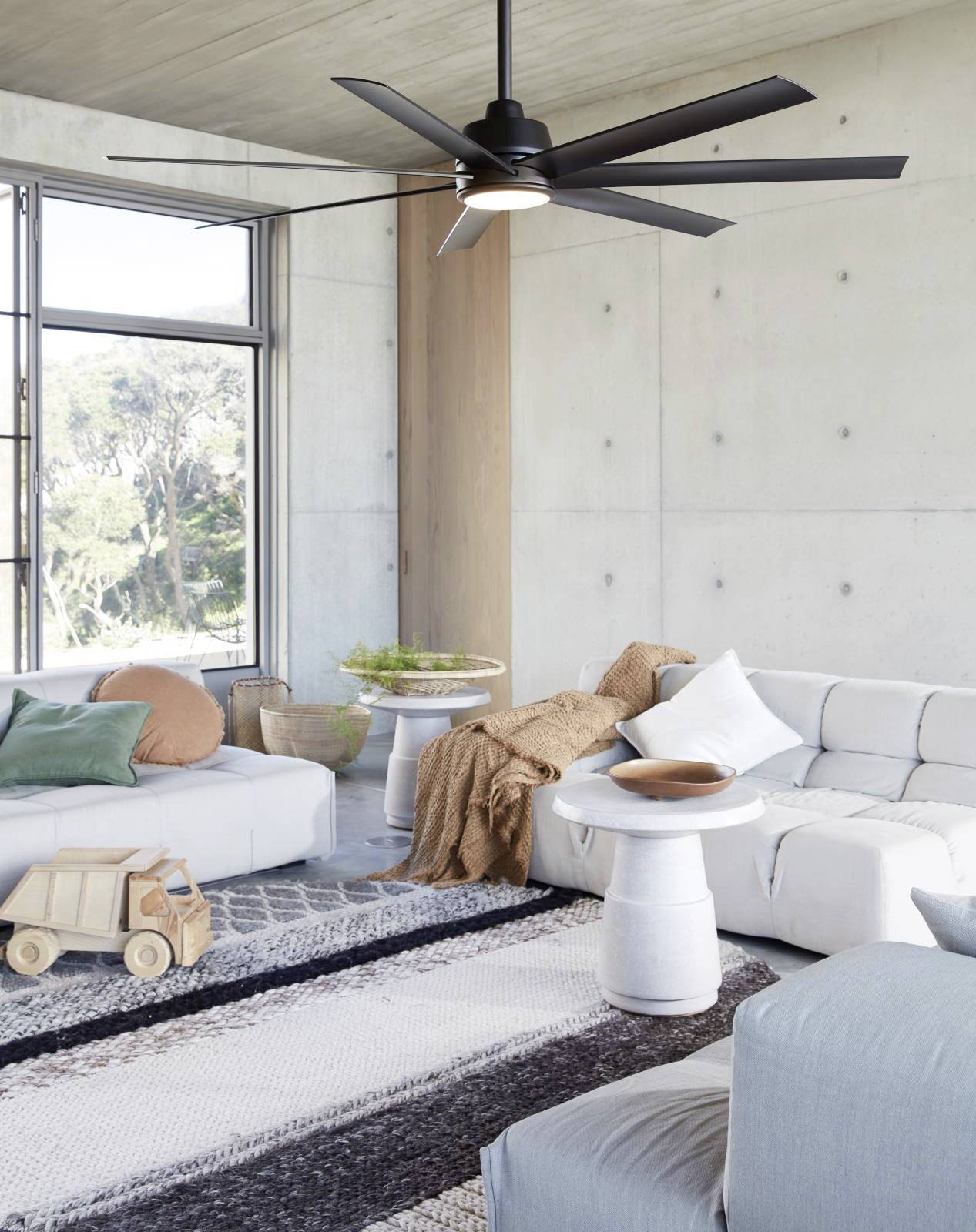 Wohnzimmer mit modernem Design: weiße Sofas, Holzelemente, großer schwarzer Deckenventilator, helle Wände, Fenster mit Naturblick.