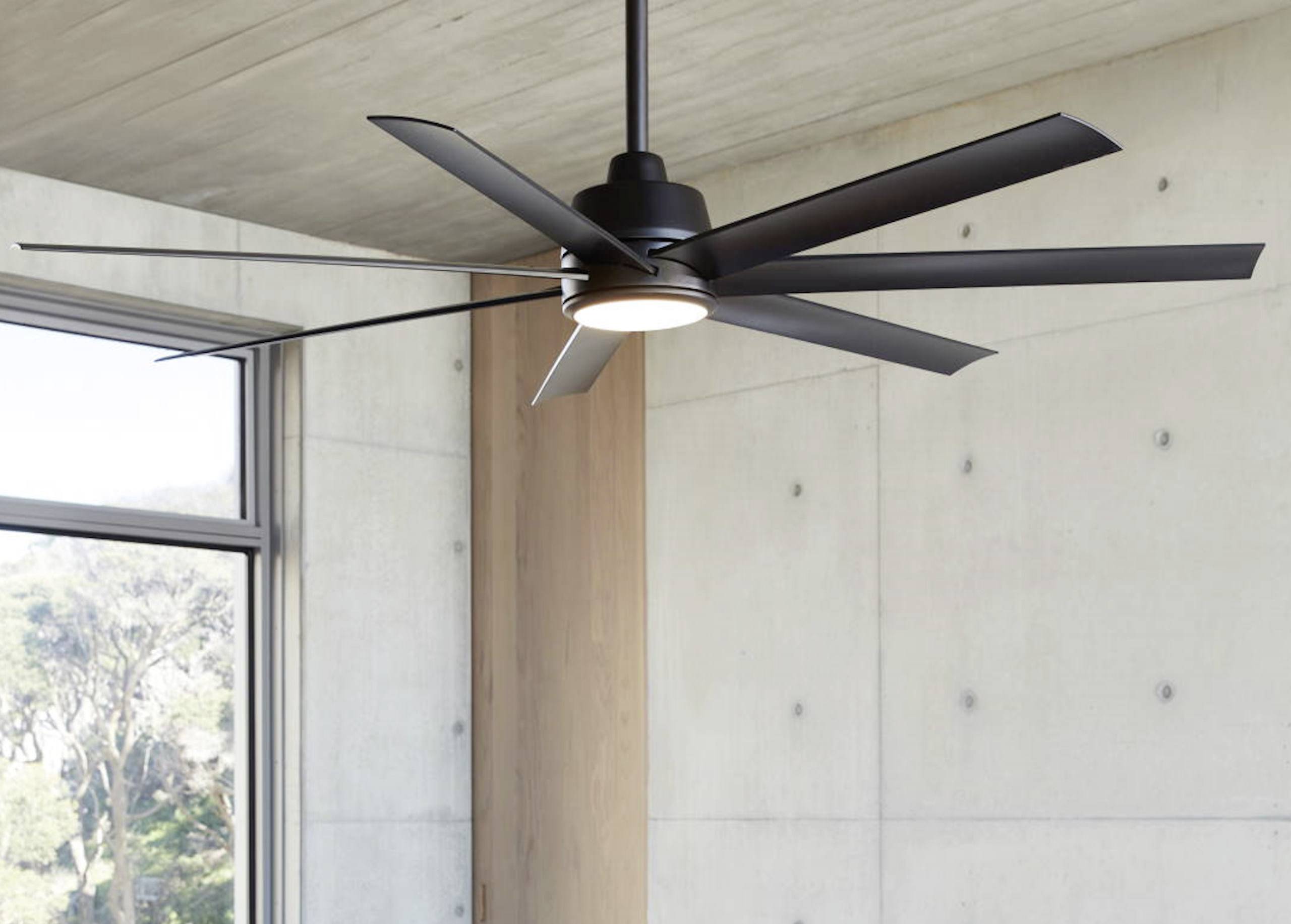 Ein moderner Deckenventilator mit mehreren Flügeln hängt an der Decke in einem hellen Raum mit großen Fenstern.