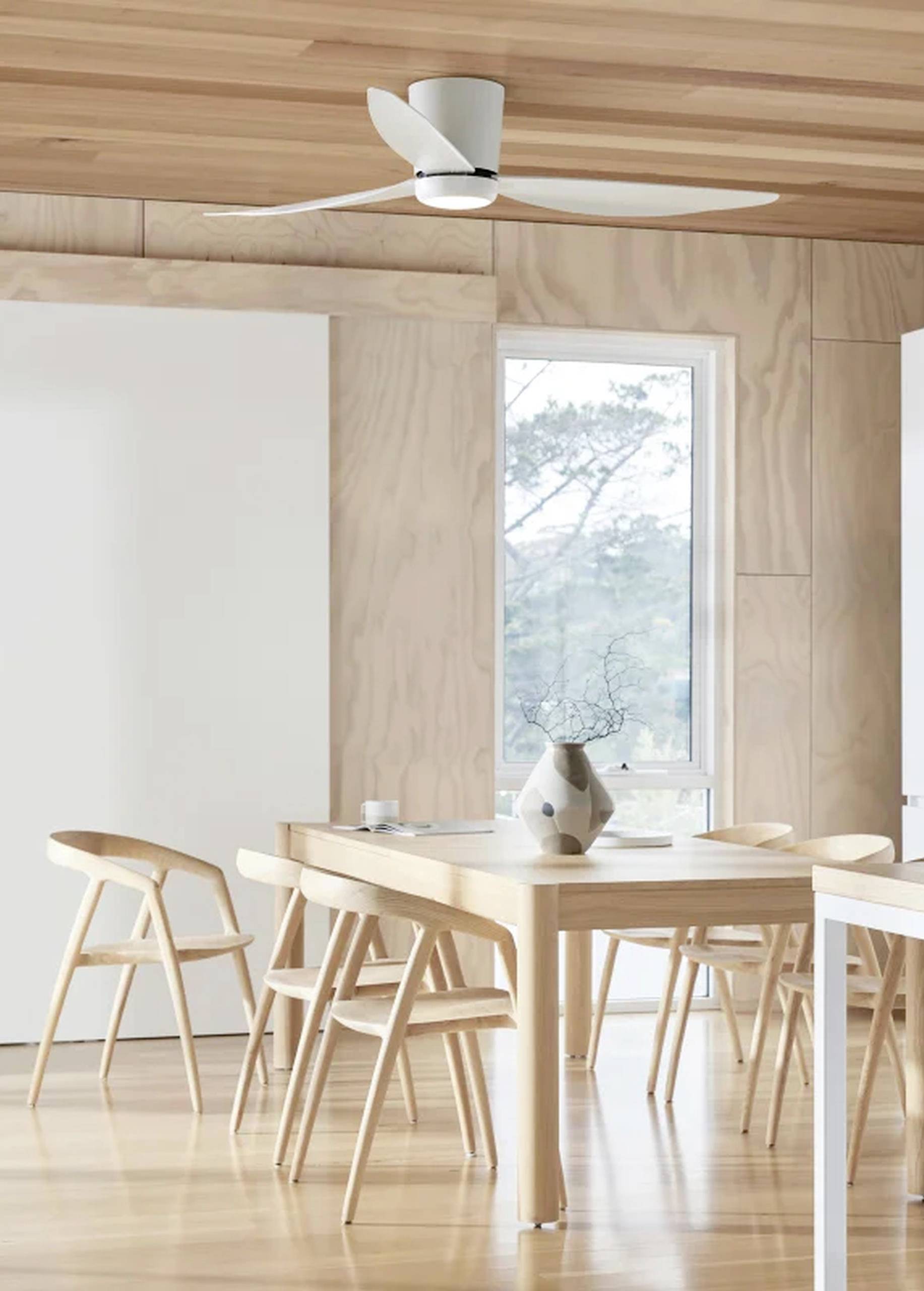 Helles Esszimmer mit Holztisch und Stühlen, Vase mit Zweig auf dem Tisch, großer Ventilator an der Holzdecke, Fenster im Hintergrund.