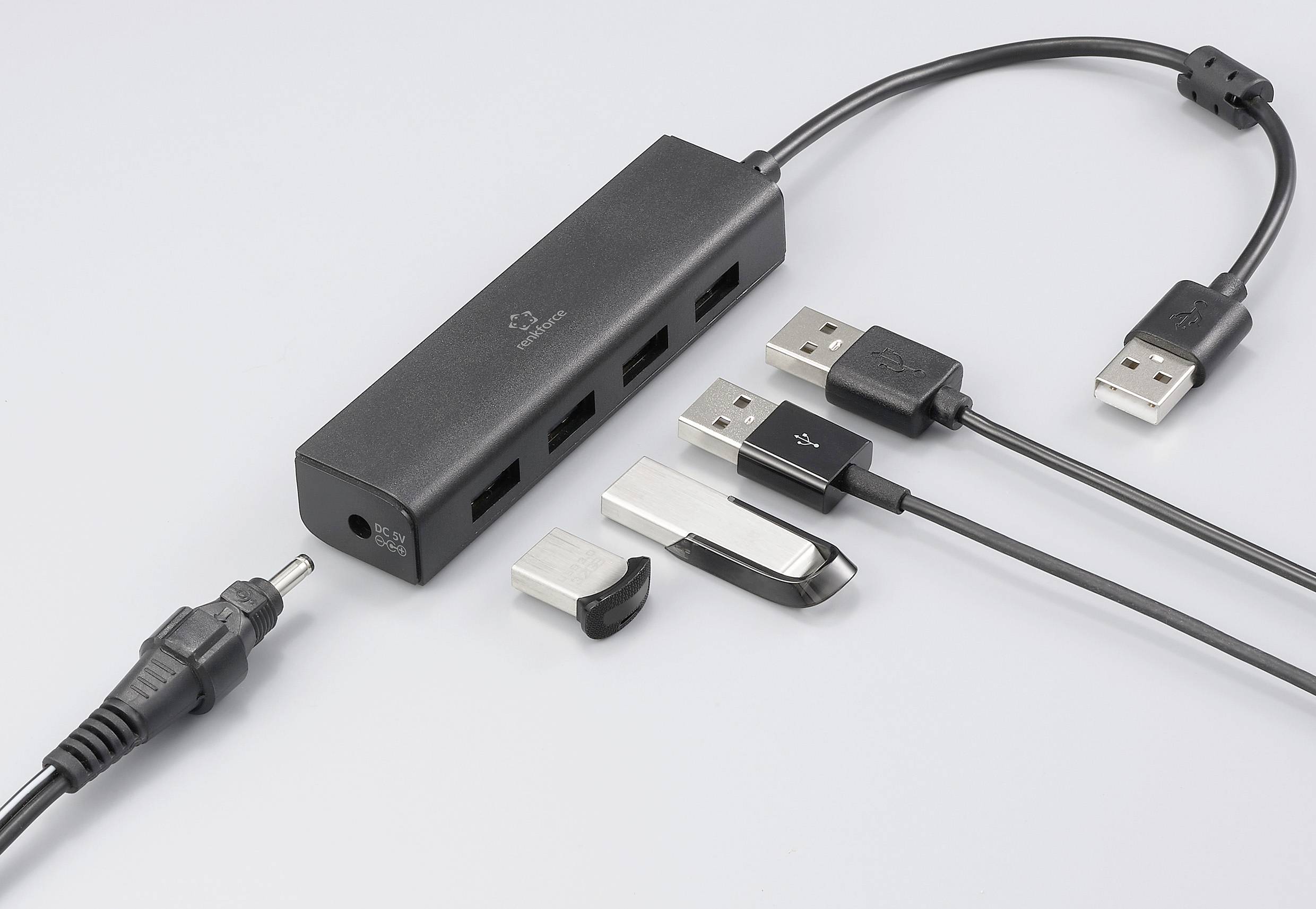 Ein USB-Hub mit vier Anschlüssen, verbunden mit USB-Kabeln und Steckern. Daneben liegt ein weiteres Kabel mit einem runden Stecker.