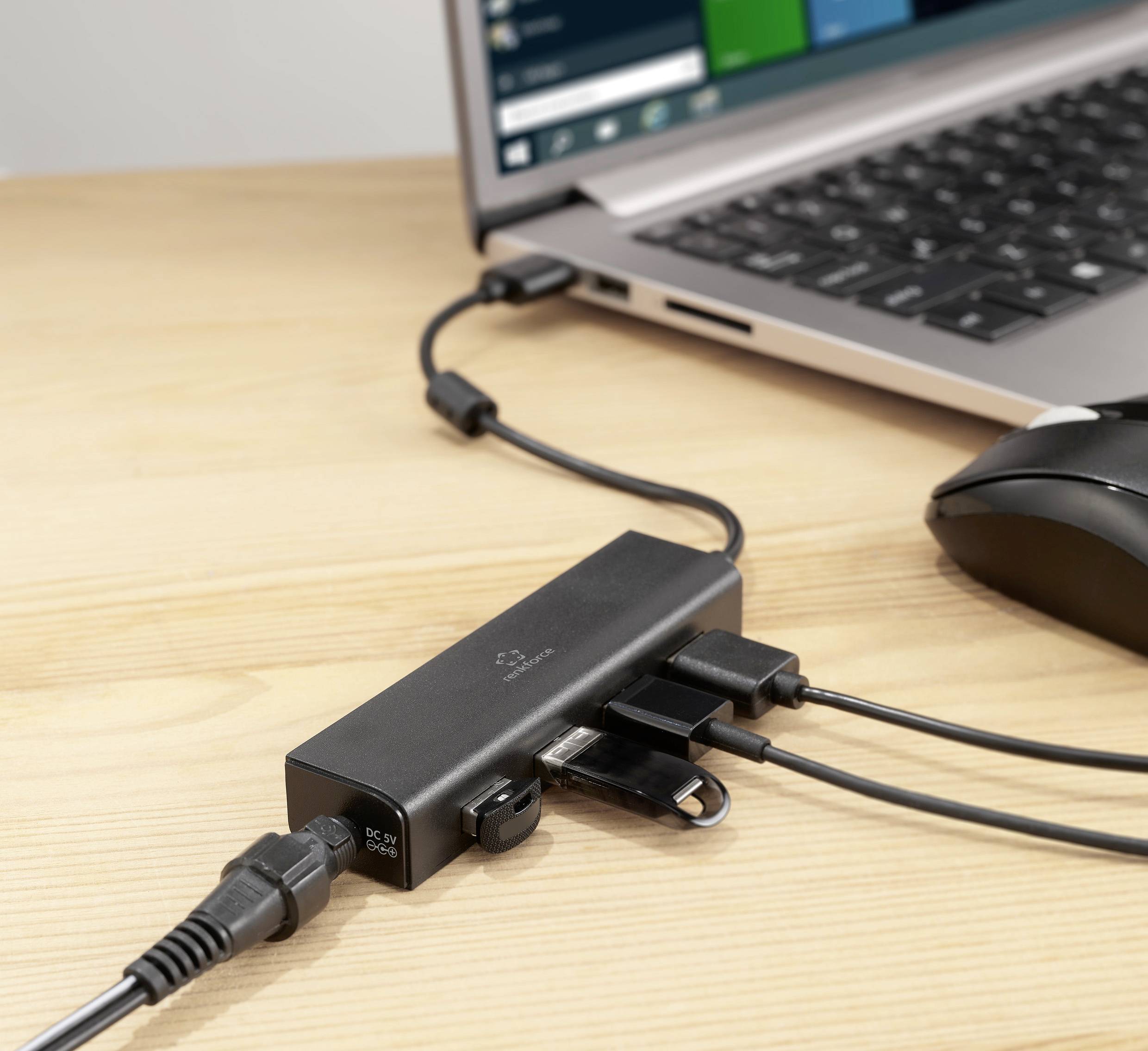 Ein Laptop ist mit einer Dockingstation verbunden, die mehrere Kabelanschlüsse bietet. Eine Computermaus ist ebenfalls angeschlossen.