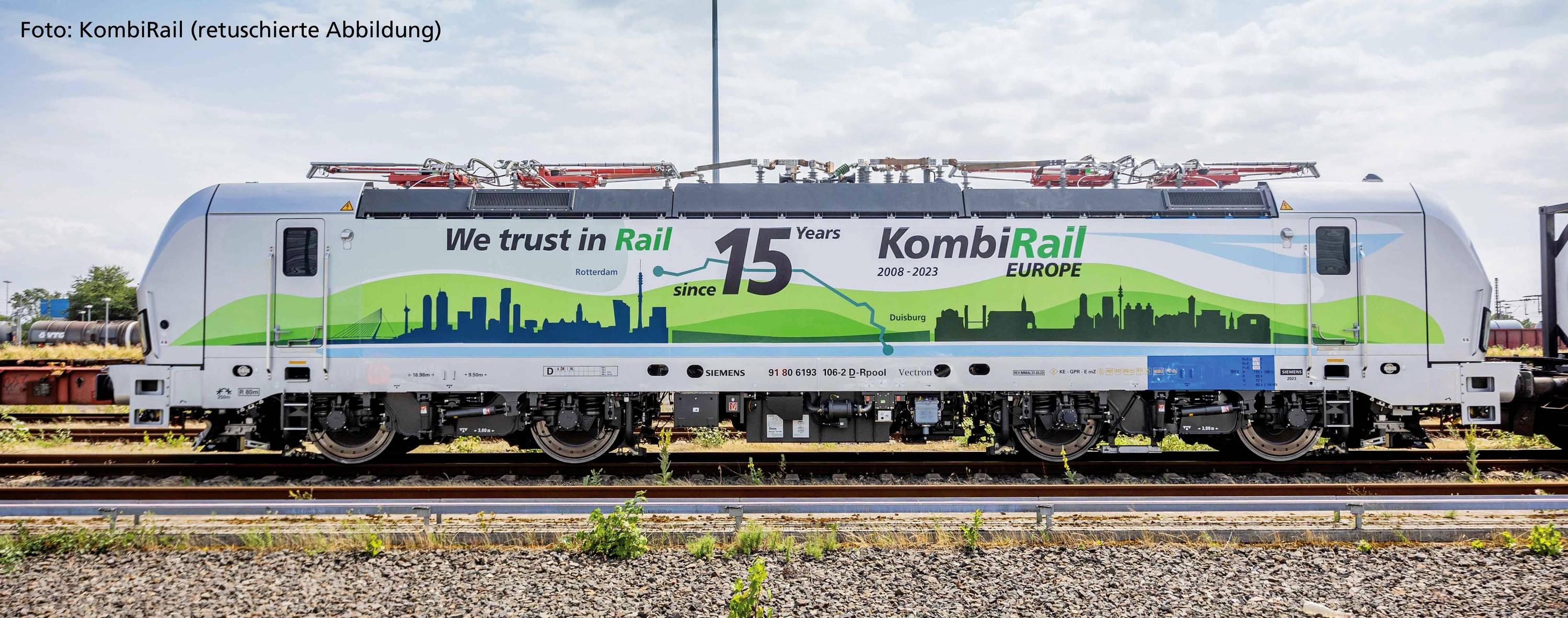 Zuglokomotive mit Aufschrift 'We trust in Rail since 15 Years KomBiRail EUROPE 2008-2023', in grüner Landschaftsgrafik gestaltet.