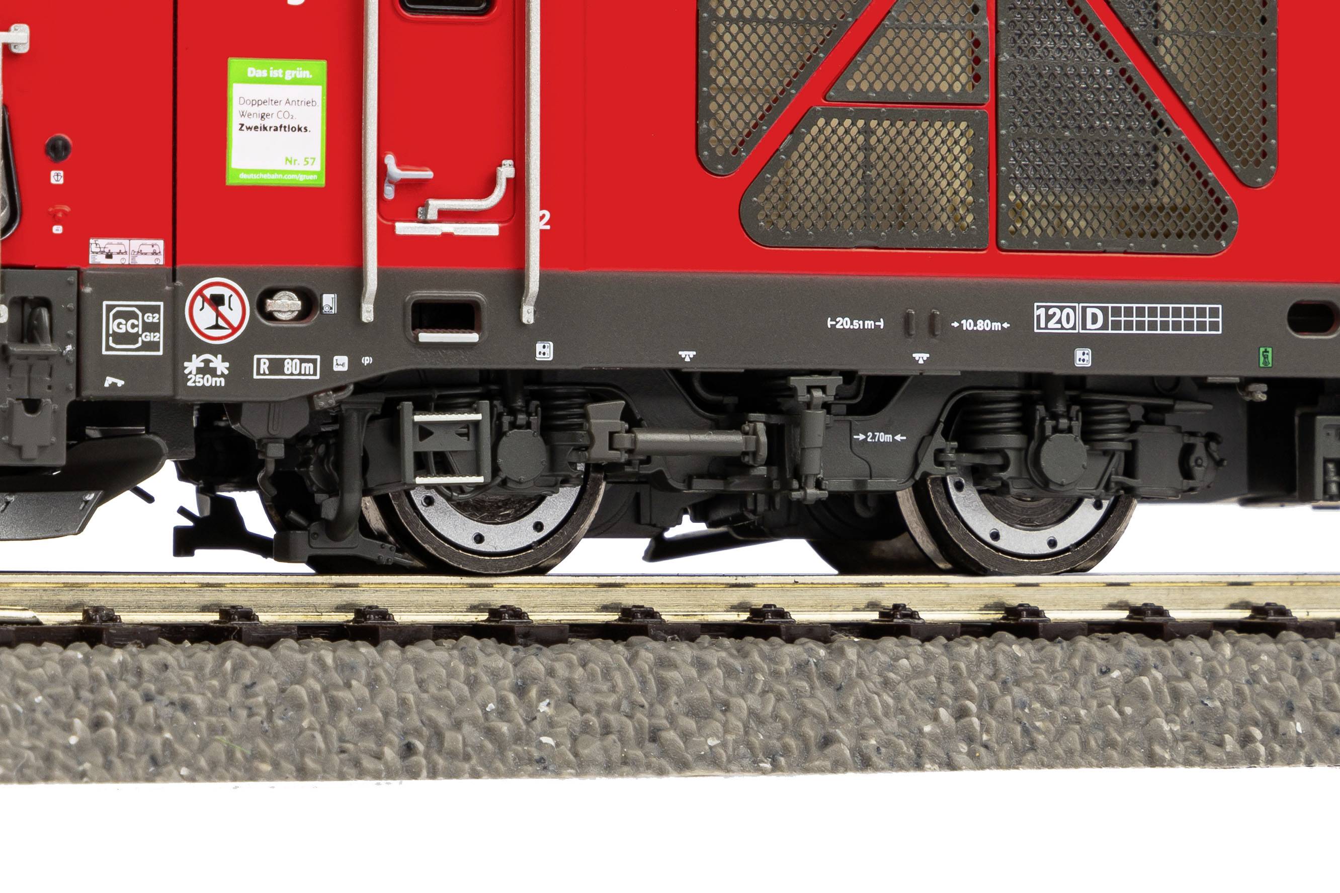 Nahaufnahme eines roten Zugwaggons zeigt Fahrwerk und Räder auf Gleisen. Schilder und Logos sind auf dem Waggon zu sehen.