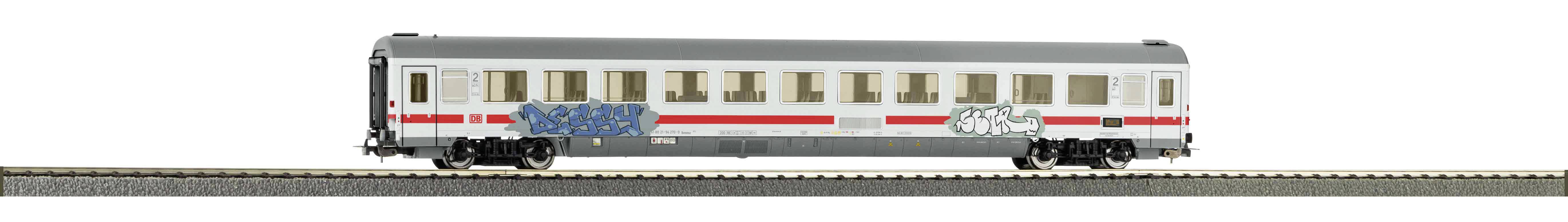 Ein weißer Zugwaggon mit roten Streifen und Graffiti. Der Wagen steht auf Schienen und hat mehrere Fenster.