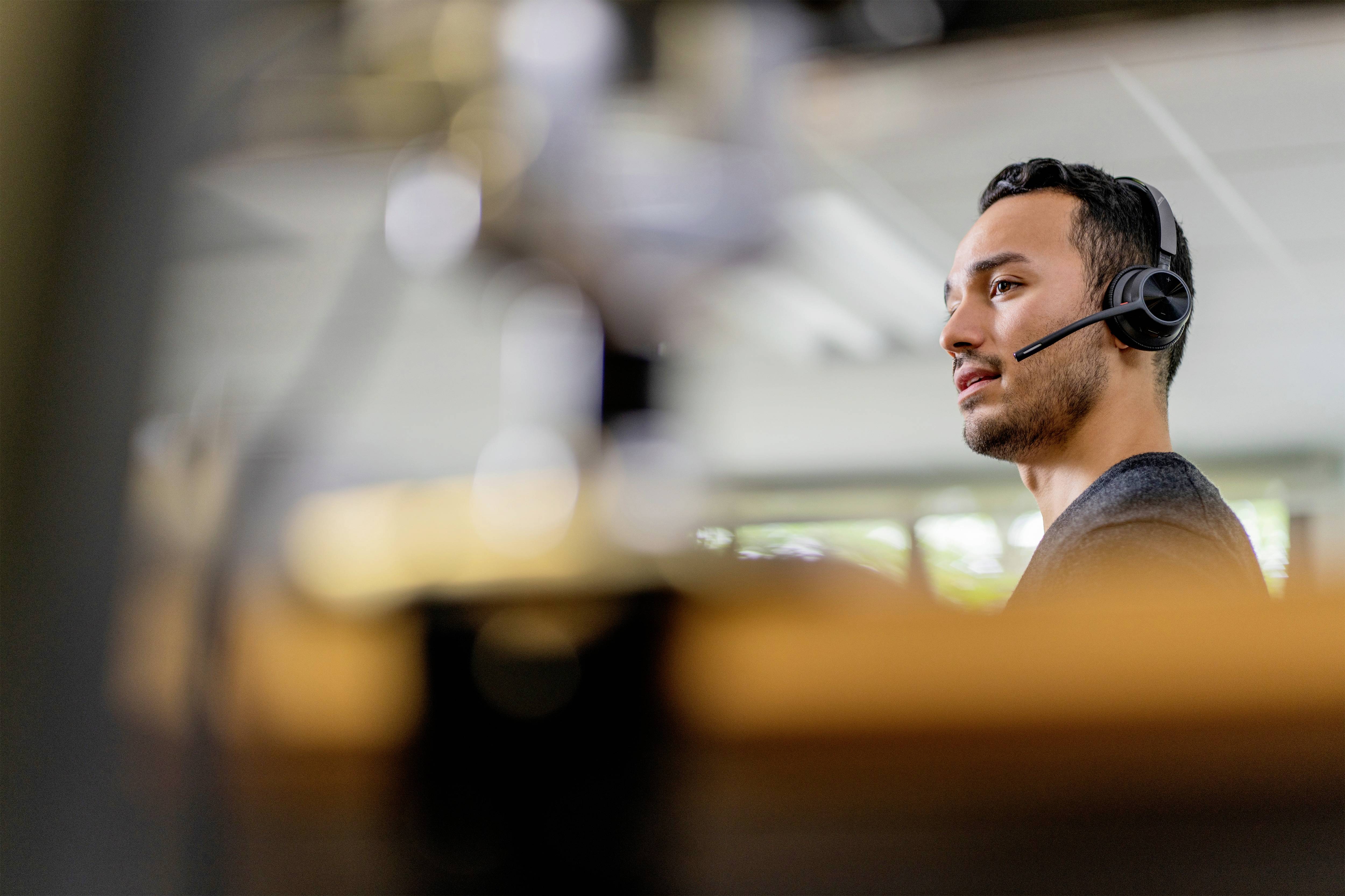 Mann mit Headset im Büro, konzentriert bei der Arbeit am Computer. Er telefoniert oder nimmt an einem virtuellen Meeting teil.