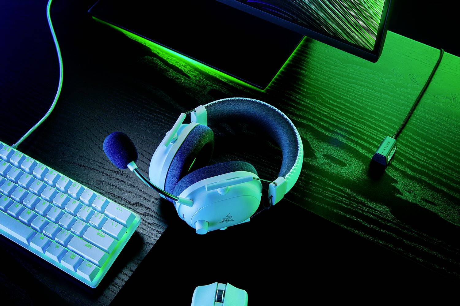 Ein weißes Gaming-Headset liegt auf einem dunklen Holztisch neben einer Tastatur und einer Computermaus, beleuchtet von grünem Licht.