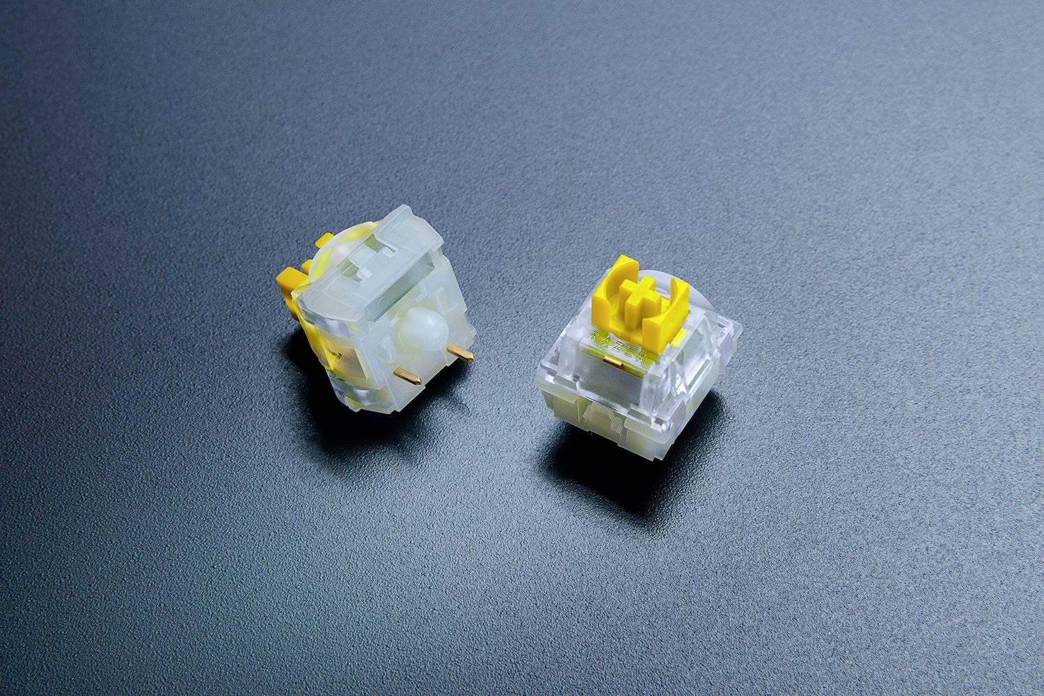 Zwei mechanische Tastaturschalter mit gelben Stößeln auf einer dunklen Oberfläche.