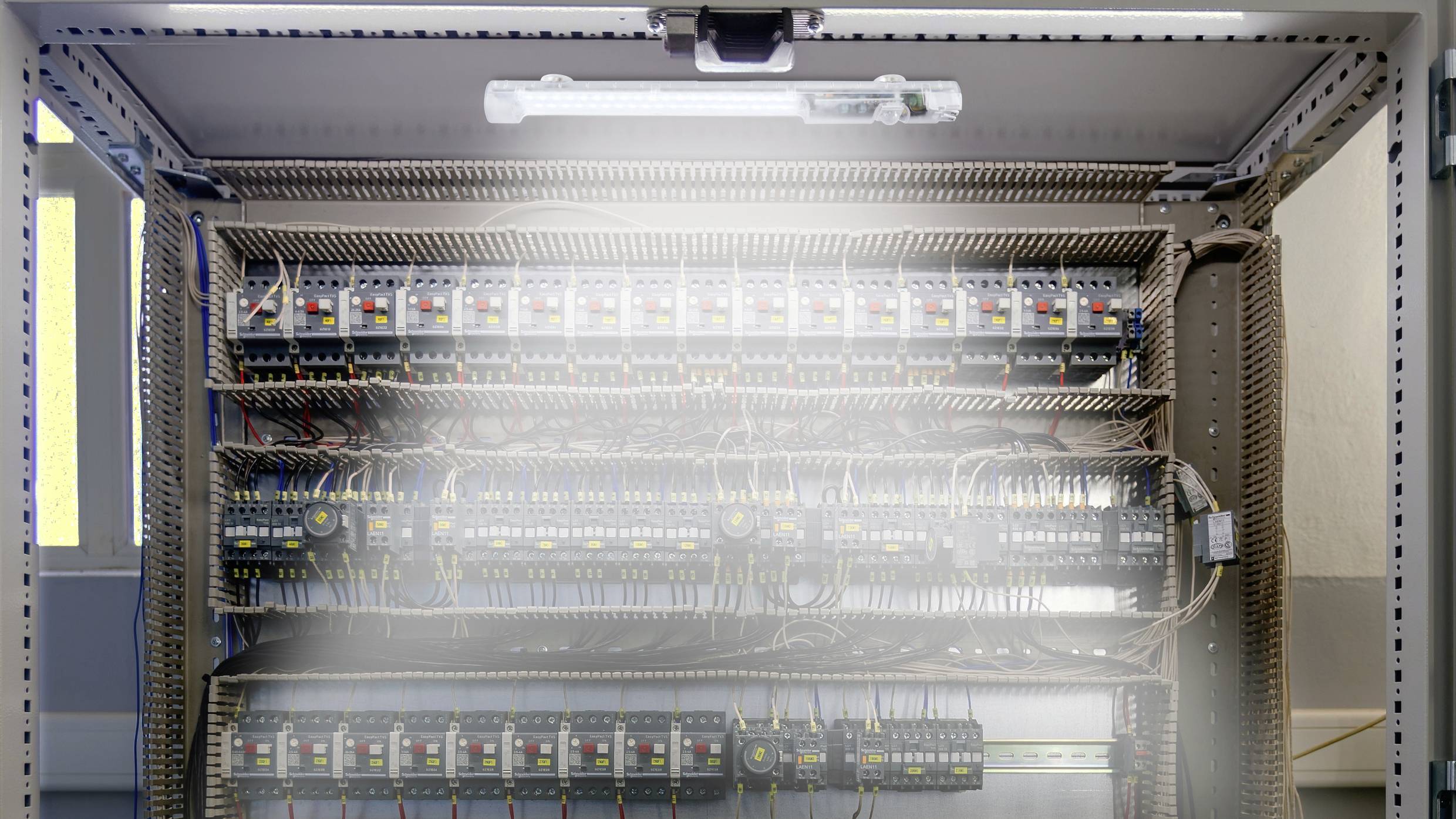 Ein geöffneter Schaltschrank mit mehreren Reihen Schaltern und verdrahteten Verbindungen, beleuchtet von einer Lampe oben.