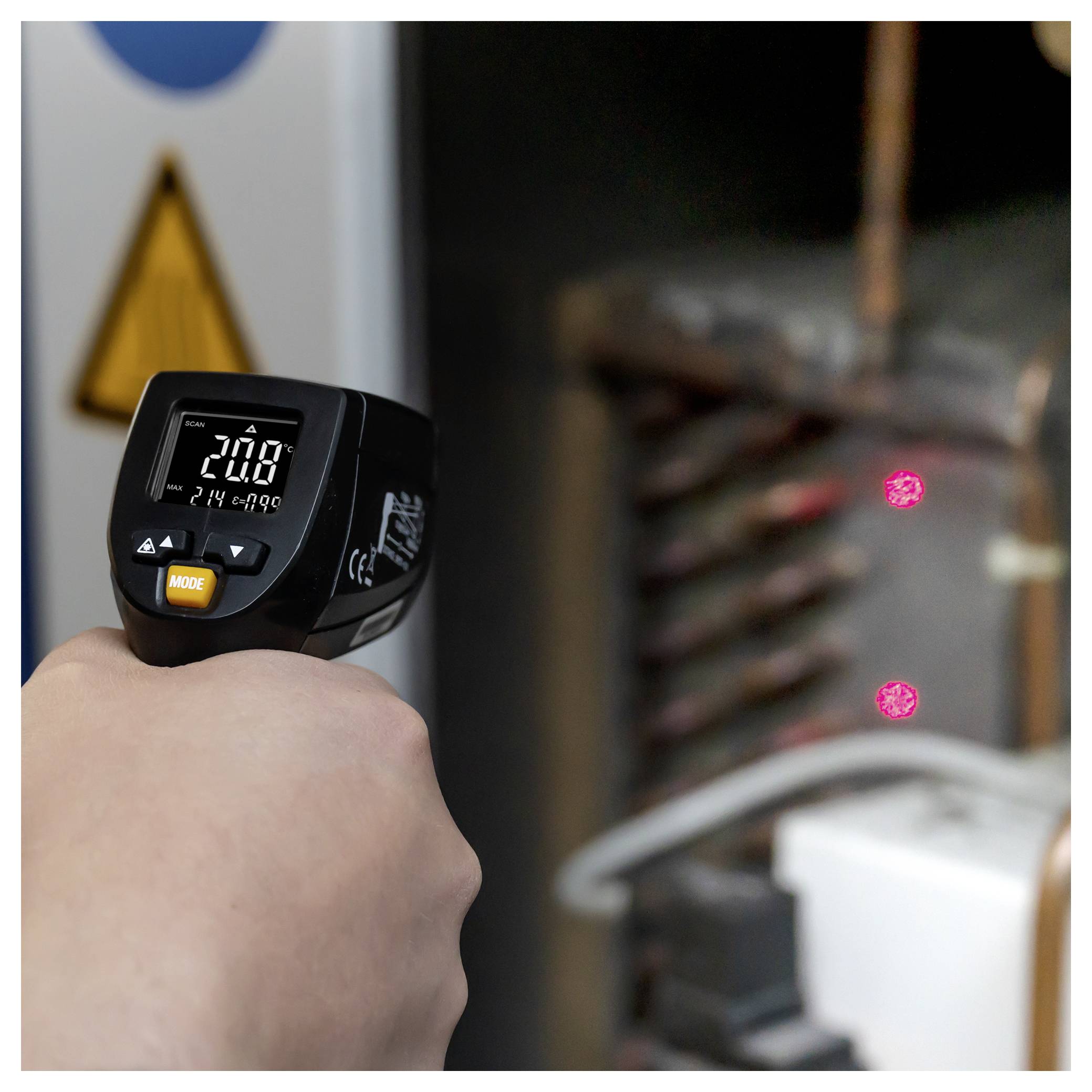Tragbares Infrarot-Thermometer, das auf Industrieausrüstung ausgerichtet ist und eine Temperaturanzeige zeigt, während rote Laserpunkte das Ziel markieren.
