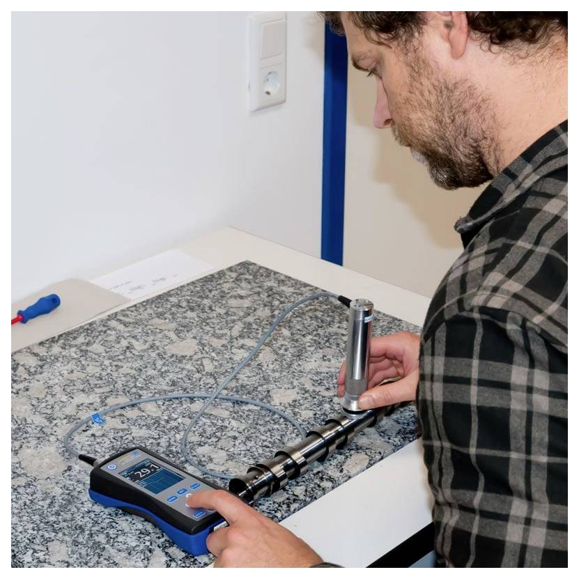 Mann, der mit einem tragbaren digitalen Messgerät und einer Sonde eine Metallrohrversammlung auf einer Werkbank prüft